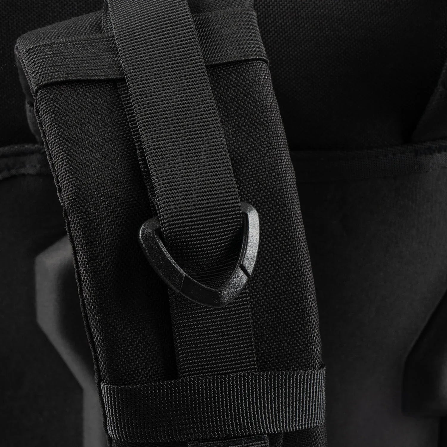 Nahaufnahme des STOIRM 40L Tactical Pack GEN2 von STOIRM mit einem schwarzen 1000D-Nylon-Gurt, der mit einem schwarzen dreieckigen Kunststoffhaken befestigt ist und die detaillierte Struktur und die Nähte der Tasche zur Geltung bringt.