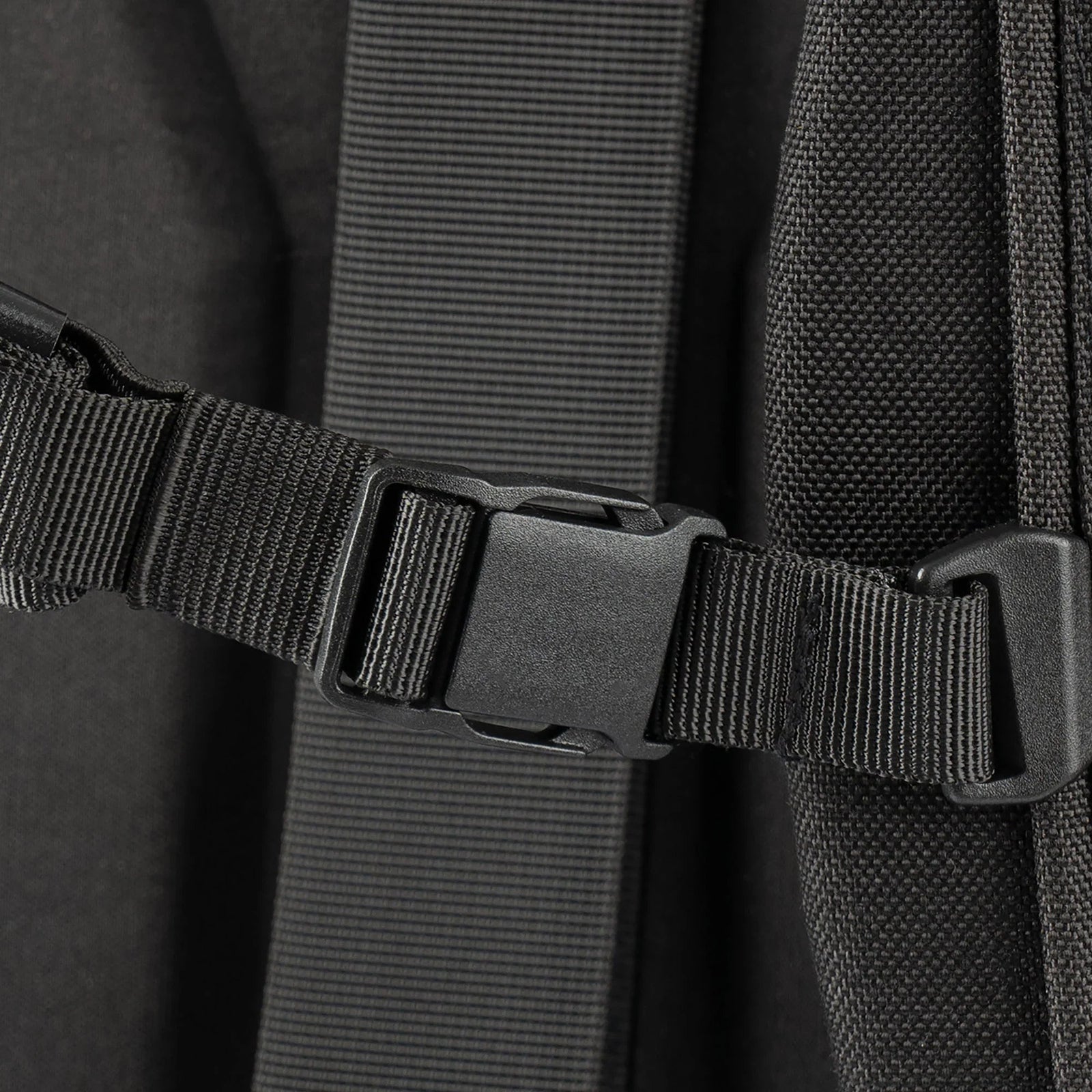Nahaufnahme einer schwarzen Kunststoffschnalle, die am strukturierten Riemen der STOIRM Messenger Bag von STOIRM befestigt ist, wobei im Hintergrund gepolstertes Material zu sehen ist.