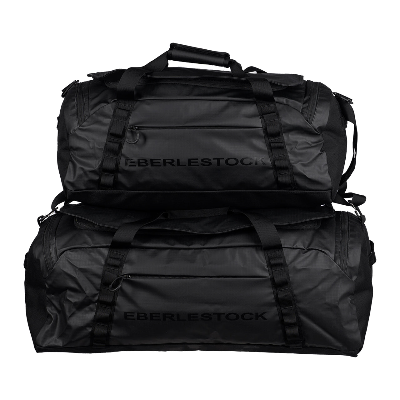 Zwei große schwarze EBERLESTOCK Hyllus Duffel 45 Taschen mit seitlichen Griffen und Reißverschlüssen sind übereinander gestapelt, mit dem auffälligen EBERLESTOCK Branding auf der Seite jeder Tasche.