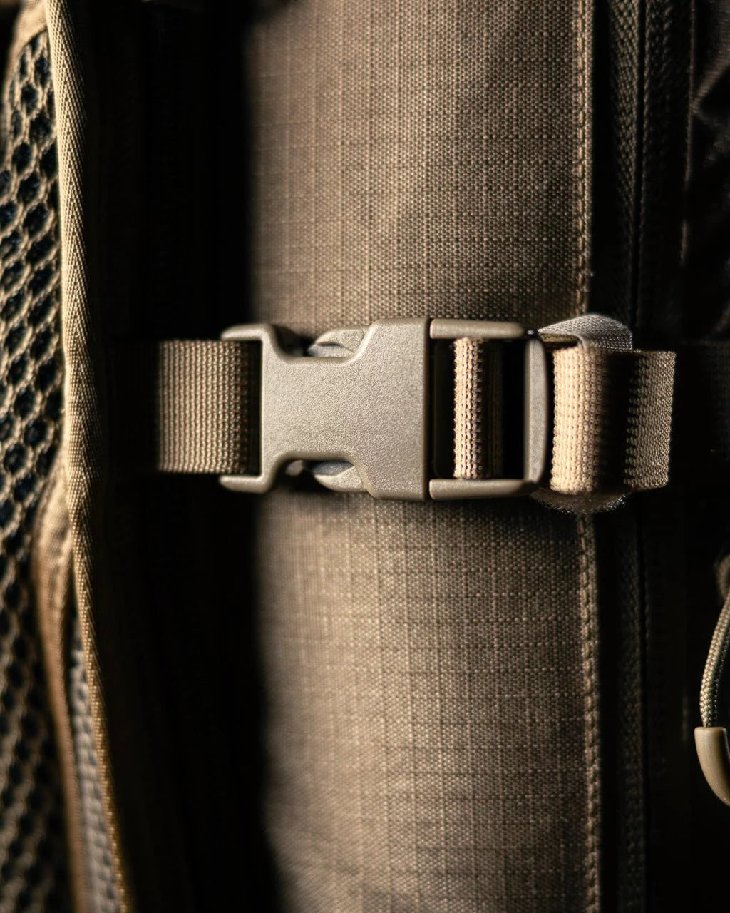 Nahaufnahme einer Kunststoffschnalle, die an einem braunen, strukturierten Rucksackgurt mit Mesh-Gewebe befestigt ist. Der Gurt ist mit dem Eberlestock Batwing V2 von EBERLESTOCK ausgestattet - ein wesentlicher Bestandteil des vielseitigen EMOD-Systems.