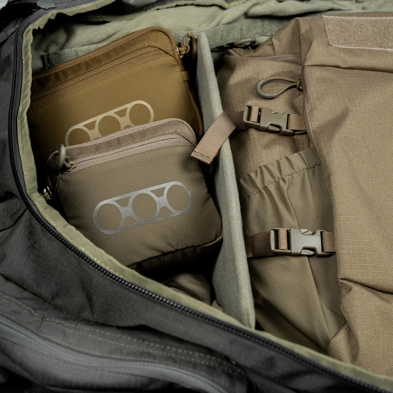 Die Nahaufnahme eines geöffneten Rucksacks zeigt zwei coyotebraune EBERLESTOCK General Purpose Pouch Large Reißverschlusstaschen mit kreisförmigem Design und organisierten Fächern mit Riemen und Taschen - ideal für MOLLE-Befestigungen.