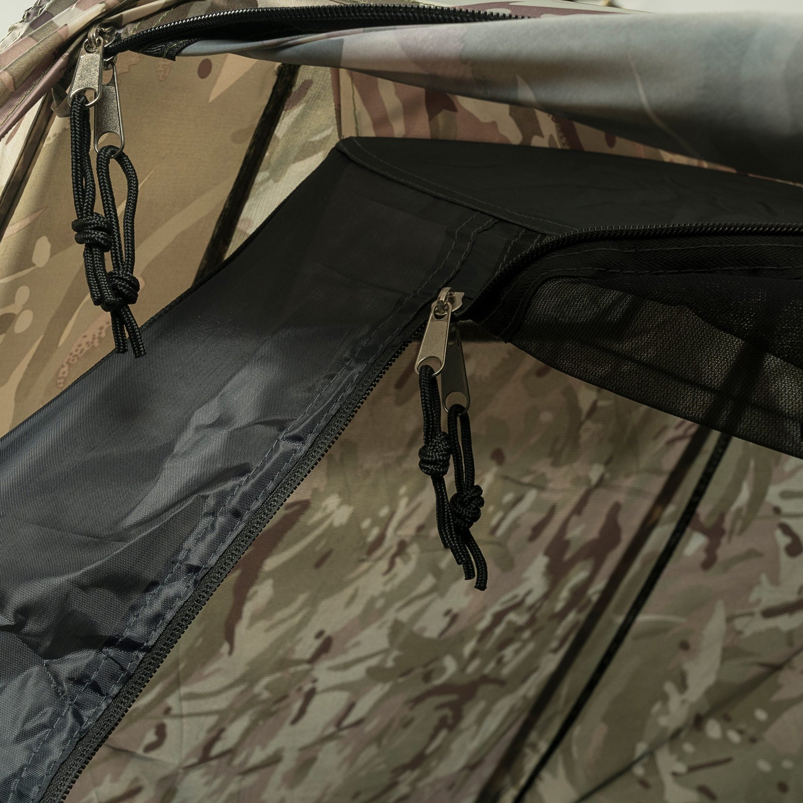 Nahaufnahme eines HIGHLANDER FORCES Highlander Zelt Blackthorn 1+ Gen2 - HMCT Trekking-Zelt mit Tarnmuster, zwei Reißverschlüssen mit Bändern, schwarzem Futter, Mesh-Gewebe und sichtbaren äußeren Stoffdetails.