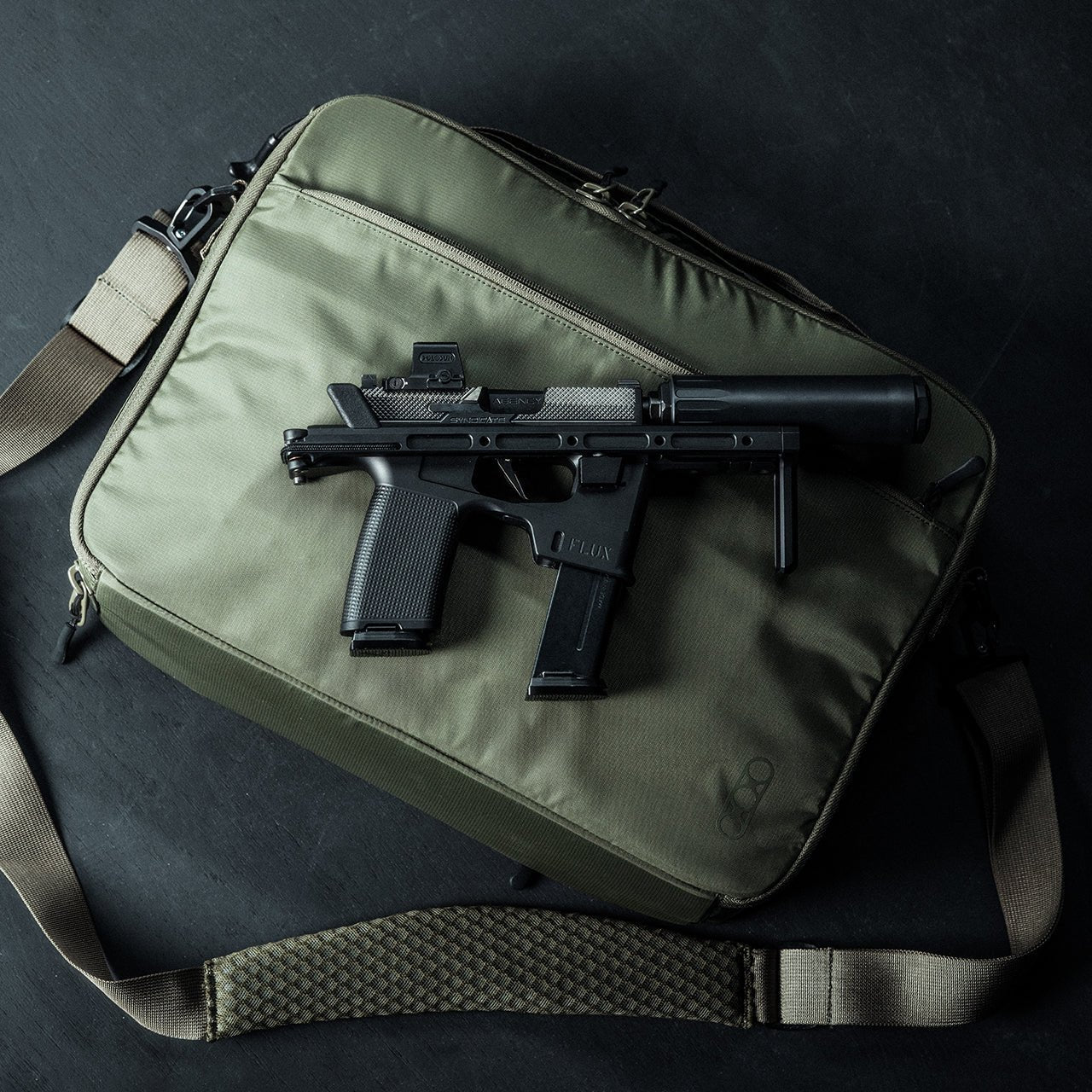 Eine kompakte schwarze Handfeuerwaffe mit verlängertem Magazin und Schalldämpfer sitzt auf einem geschlossenen olivgrünen EBERLESTOCK Fade Brief mit hellbraunem Riemen vor einem dunklen Hintergrund, der an Szenen aus der zivilen Polizeiarbeit erinnert.