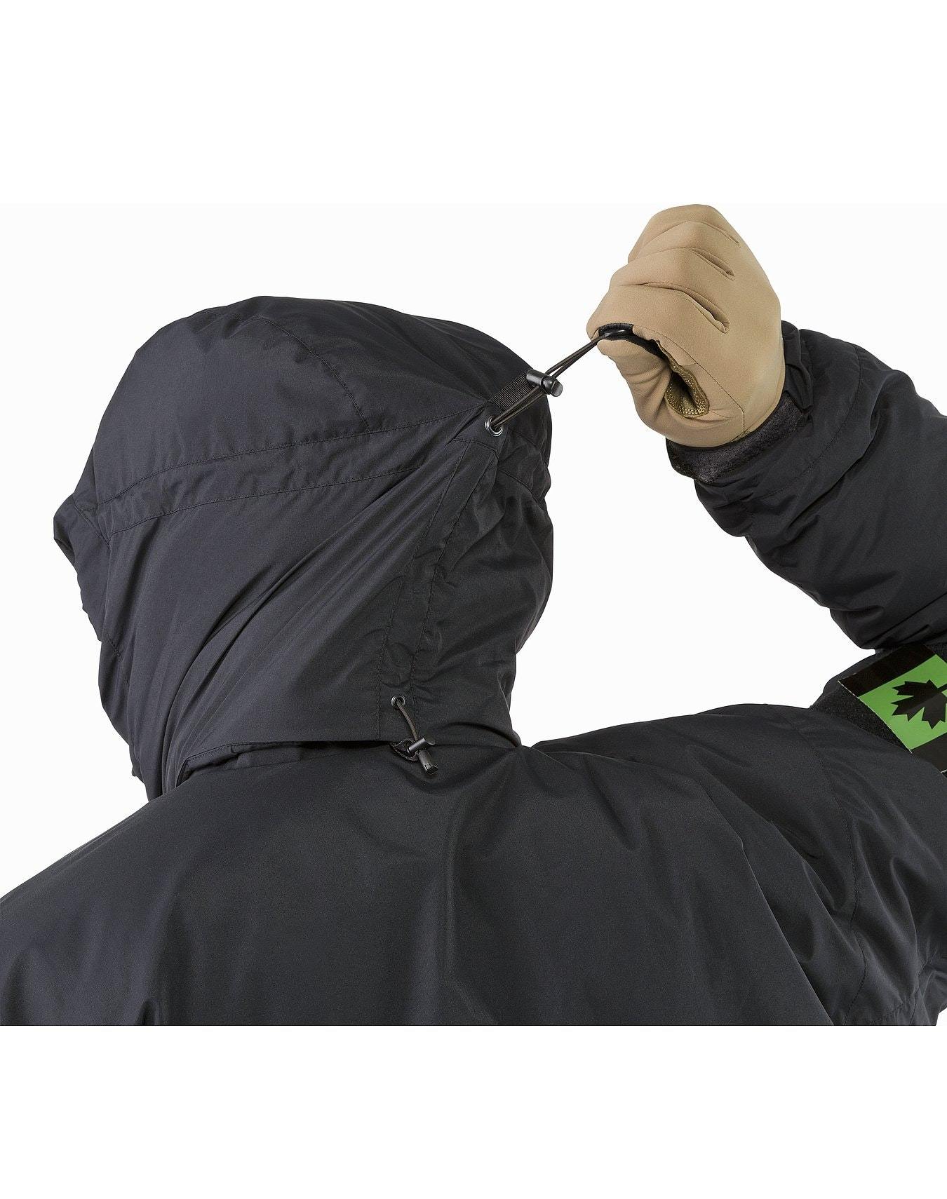 Eine Person mit hellbraunen Handschuhen verstellt den Kapuzenzug einer schwarzen ARC'TERYX LEAF Arc'teryx Cold WX Jacket SV Gen1.4, in der Rückenansicht vor weißem Hintergrund.