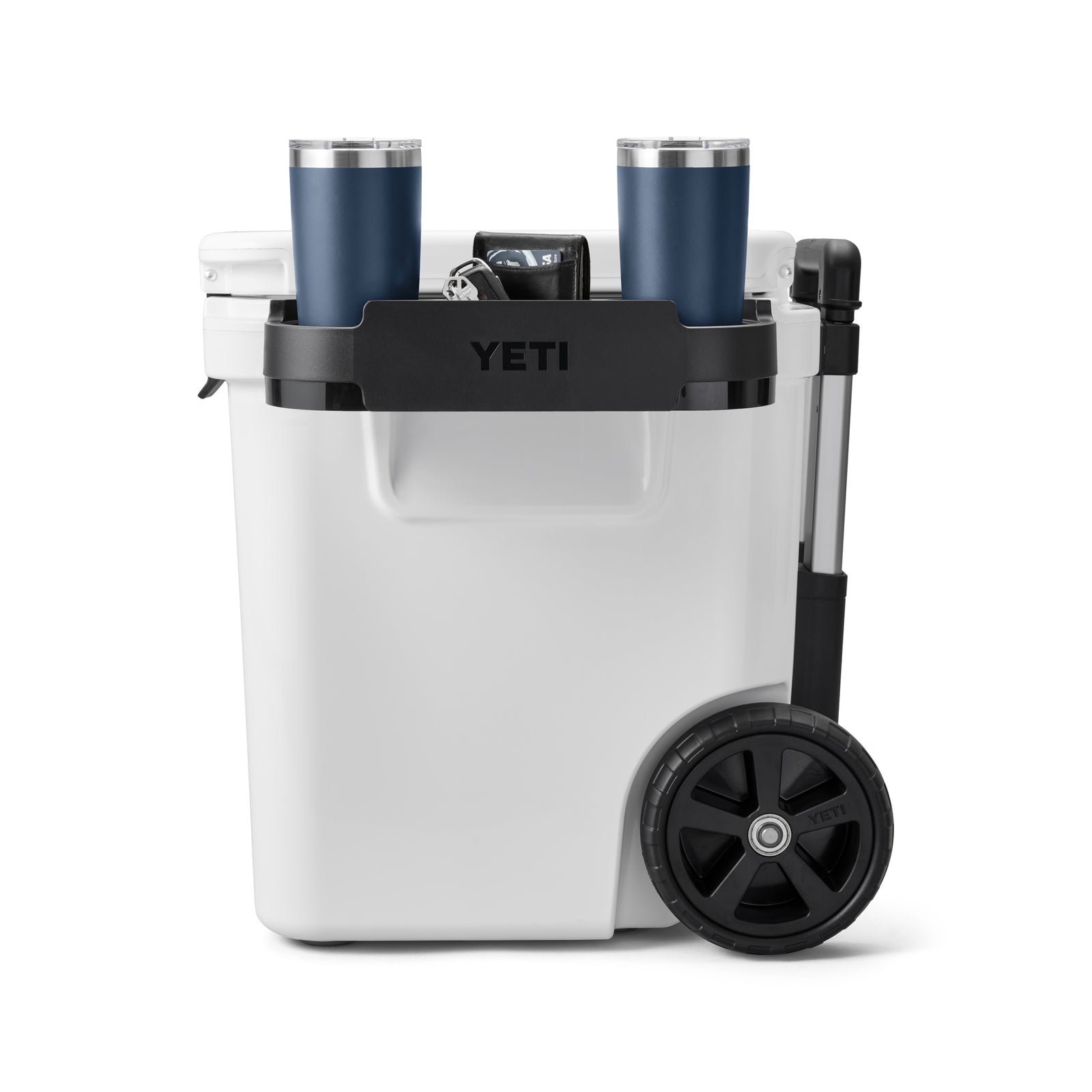 Die weiße YETI® Kühlbox Roadie 60 hat einen schwarzen Griff, einen schwarzen Deckel mit zwei blauen Reisebechern und zwei große schwarze Räder auf einer Seite für den einfachen Transport.