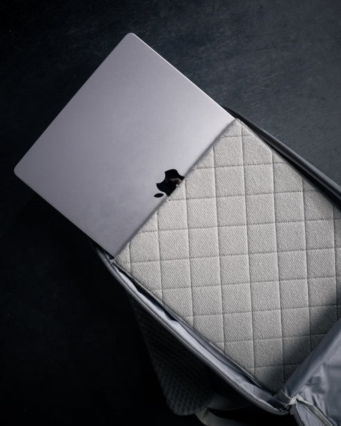 Ein silberner Laptop mit sichtbarem Apple-Logo steckt teilweise in einer gesteppten grauen Hülle in einem offenen EBERLESTOCK Eberlestock Fade Sling XL, ideal für den täglichen Gebrauch, vor einem dunklen Hintergrund.