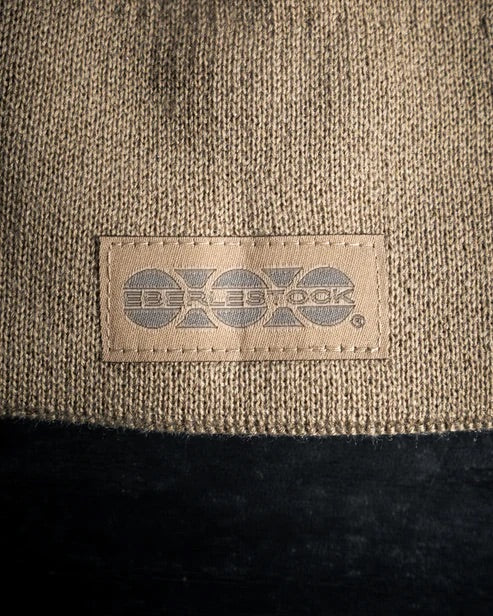 Eine Nahaufnahme der EBERLESTOCK North Fork Merino Beanie in Braun mit beigem Etikett, grauem Branding und schwarzem Kontrastrand - eine ideale Outdoor-Mütze.