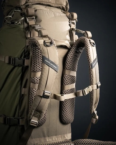 Nahaufnahme eines braunen und olivgrünen EBERLESTOCK Brute 4500, eines modularen Rucksacks mit gepolsterten, belüfteten Schultergurten und mehreren Verstellmöglichkeiten. Das EBERLESTOCK-Logo ist auf dem Gurt vor einem dunklen Hintergrund zu sehen.