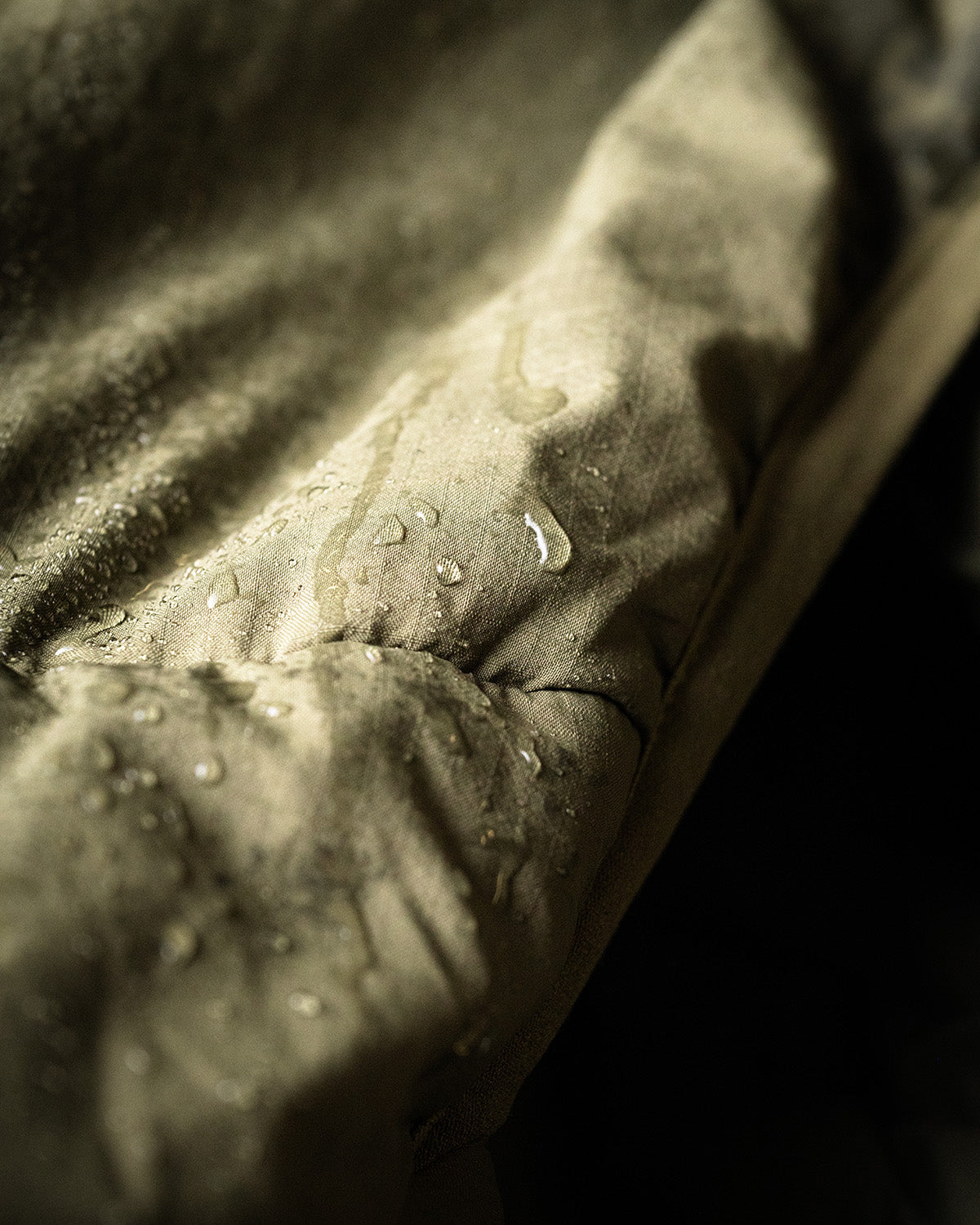 Nahaufnahme von Wassertropfen auf der EBERLESTOCK Alturas Hooded Jacket - Gunmetal, die die wasserabweisende Oberfläche der Jacke hervorheben.