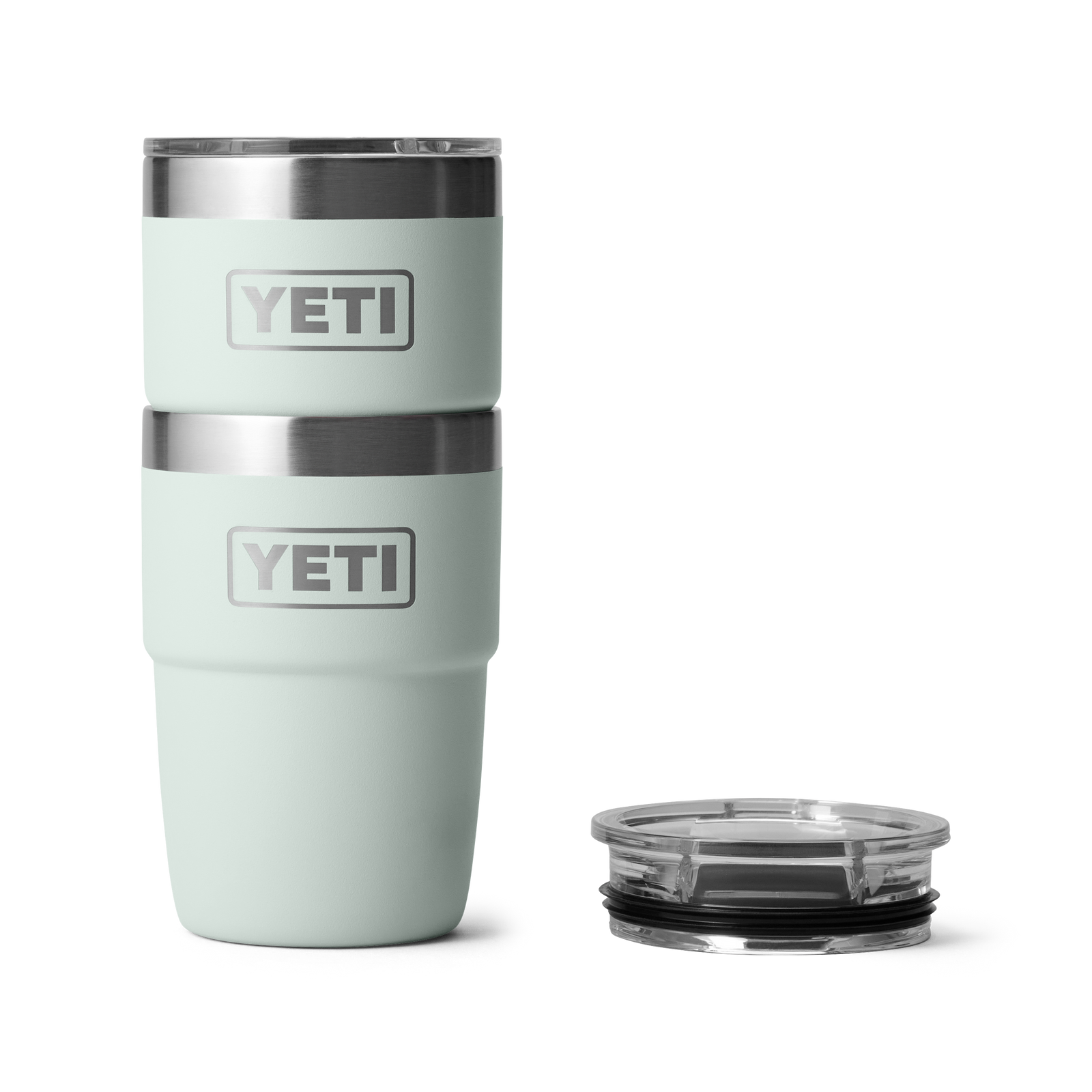 Zwei hellgraue YETI® Stapelbarer Becher Rambler 8 Oz - Ridgeline sind übereinandergestapelt, neben einem klaren Kunststoffdeckel, vor weißem Hintergrund platziert.