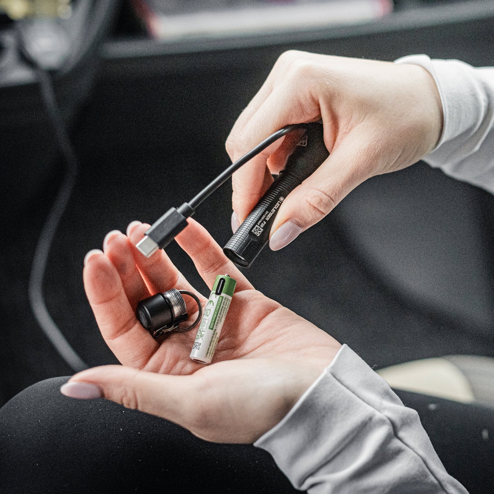 Eine Person hält eine LEDLENSER Ledlenser Taschenlampe P3R, ein Ladekabel und eine wiederaufladbare Batterie in der Hand und bereitet sich darauf vor, die Batterie zum Aufladen an die P3R-Taschenlampe anzuschließen.