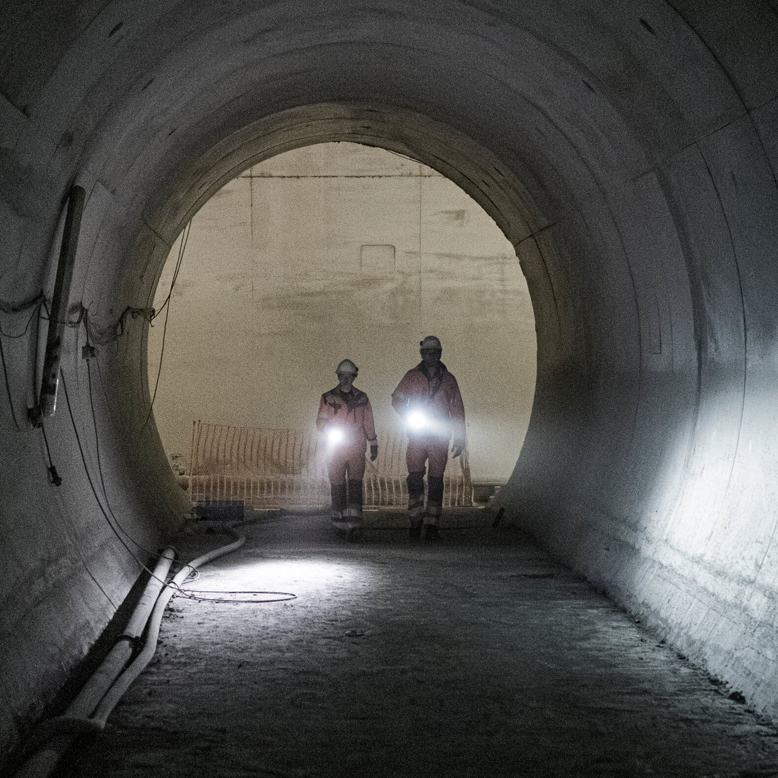 Zwei Bauarbeiter mit Helmen und Schutzwesten gehen durch einen großen, schwach beleuchteten Tunnel und halten dabei helle LEDLENSER Ledlenser Taschenlampen P7R Pro, die ideal für raue Umgebungen im Freien sind.