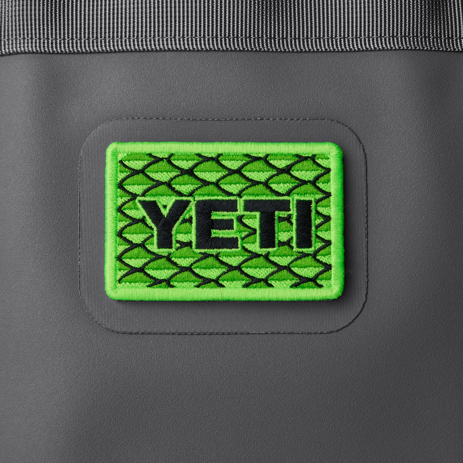 Das YETI® Scales Patch von YETI zeigt ein neongrünes und schwarzes Fischschuppenmuster, das auf dunkelgrauen Stoff gestickt ist - ideal als Klettaufnäher zur Personalisierung Ihrer Outdoor-Ausrüstung.