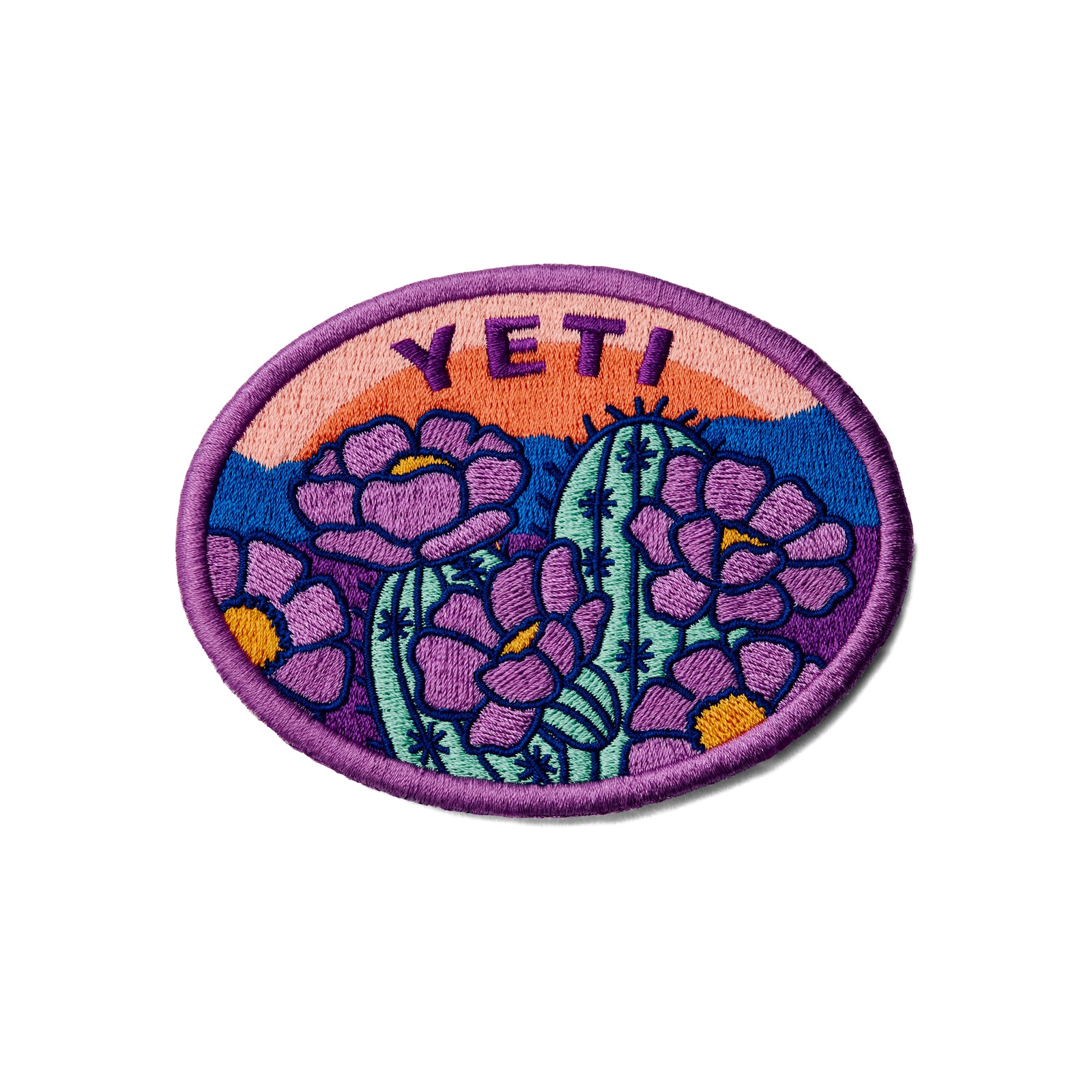Das YETI® Full Bloom Patch von YETI zeigt gestickte lila Kakteenblüten und grüne Kakteen auf einem orangefarbenen, rosa und blauen Sonnenuntergangshintergrund mit lila Umrandung. Ausgestattet mit einem Klettverschluss auf der Rückseite ist es perfekt für Ihre Outdoor-Ausrüstung.