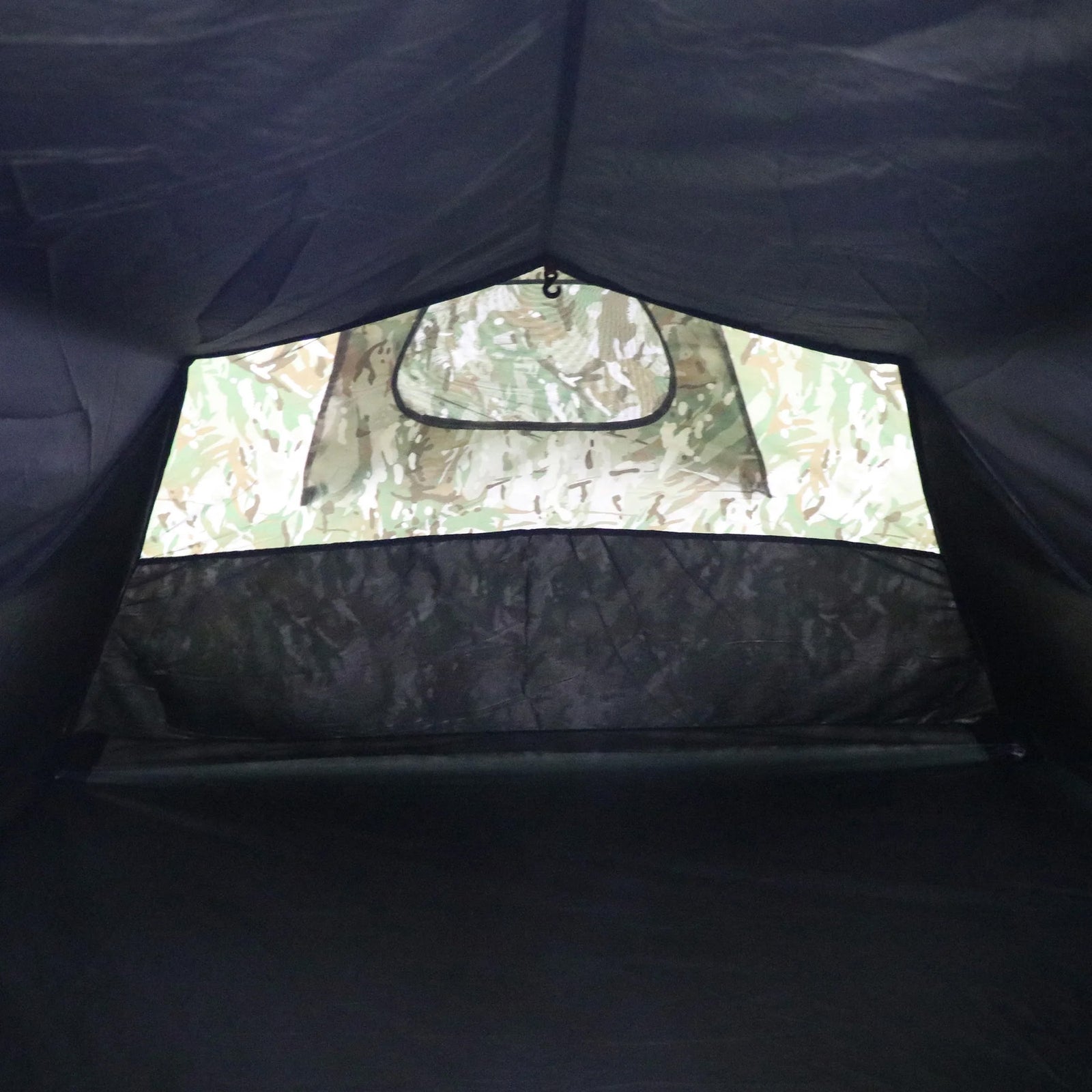 Innenansicht des Highlander Zelt BLACKTHORN 2 GEN2 - HMTC von HIGHLANDER FORCES mit einem Eingang mit Tarnmuster, einem schwarzen Netzgitter und einfallendem Licht - ein Kontrast zwischen dem dunklen Innenraum und dem hellen Äußeren dieses 2-Personen-Zeltes.