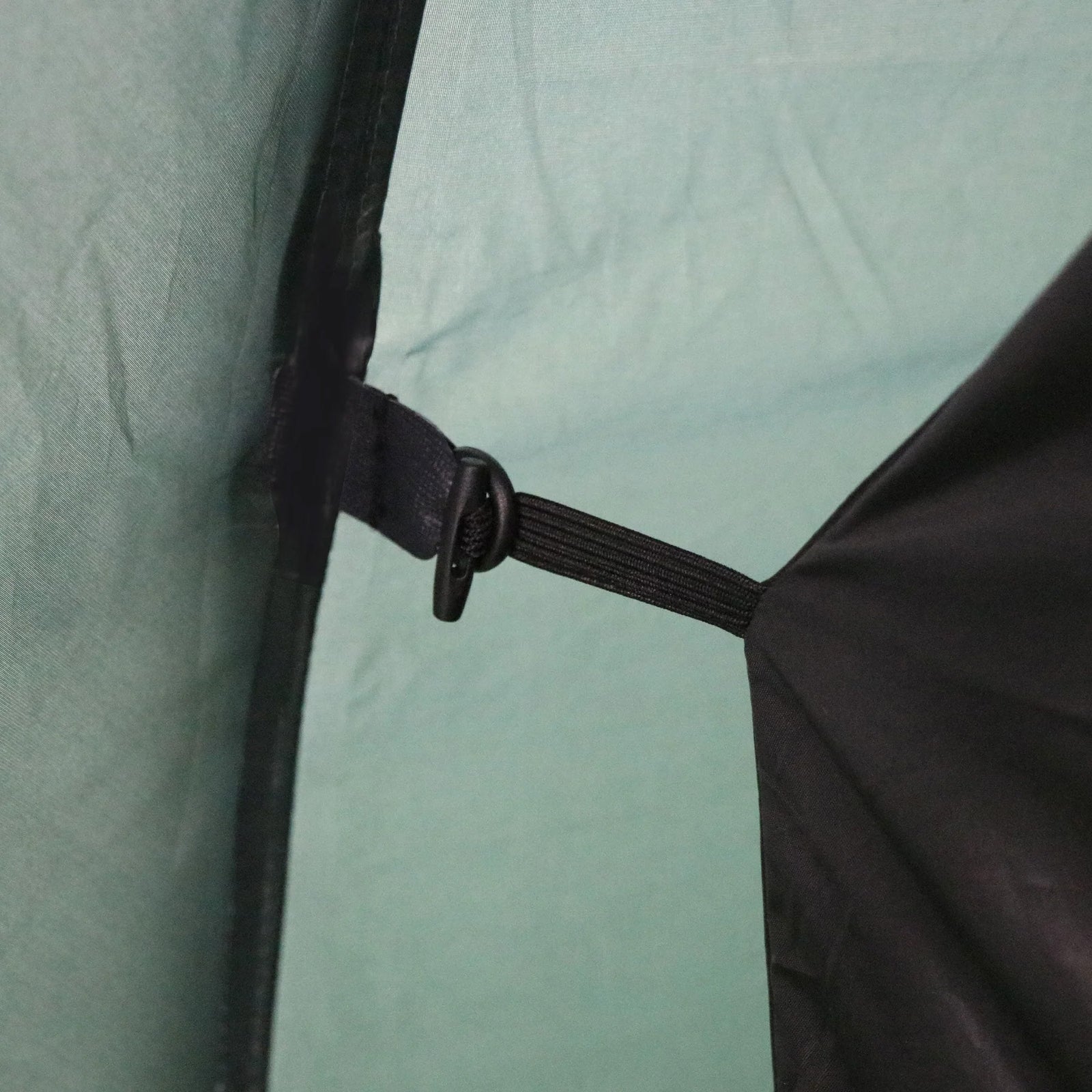 Nahaufnahme eines schwarzen Riemens und eines Kunststoffhakens, mit denen eine schwarze Klappe im Inneren des hellgrünen HIGHLANDER FORCES Highlander Zelt BLACKTHORN 2 GEN2 befestigt wird, die Teil der Innenstruktur des Trekkingzelts ist.