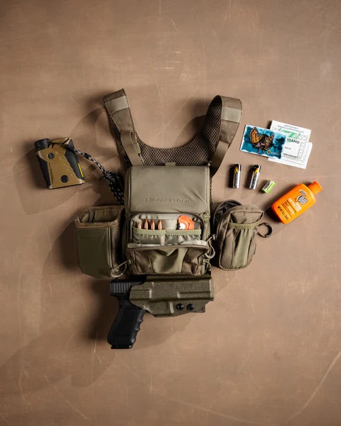 Olivgrüne taktische Weste mit Vorräten - Taschenmesser, Schrotpatronen, Taschenlampe, Sonnencreme, Batterien, Jagdmarken - auf einer braunen Oberfläche. Mit Jagdausrüstung und einem EBERLESTOCK Recon Modular Bino Pack Large für Ihr Fernglas.