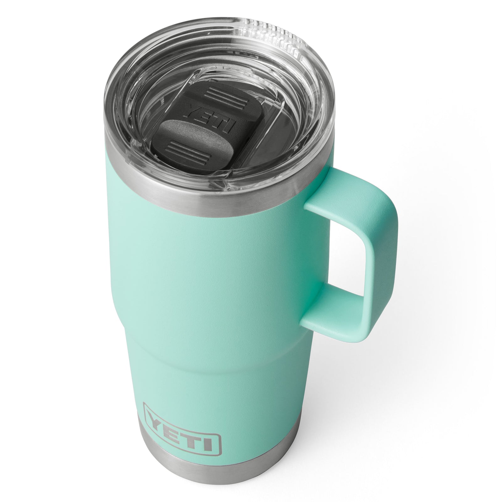 Ein YETI® Reisebecher Rambler 20 Oz in Seafoam mit durchsichtigem Deckel, schwarzem Schieber, Griff und Edelstahlrand wird aus einem leicht überhöhten Winkel auf weißem Hintergrund gezeigt.