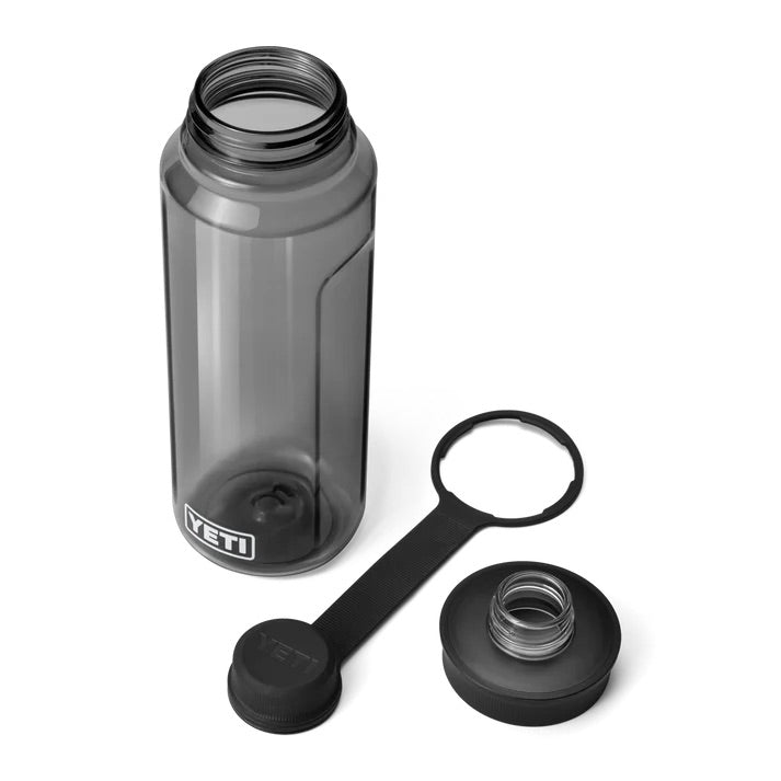 Eine transparente, graue YETI® Yonder™ 1L Wasserflasche mit abnehmbarem Deckel und angebundenem Verschluss ist auf weißem Hintergrund abgebildet. Die bruchsichere, BPA-freie Flasche hat eine breite Öffnung und trägt das YETI-Logo in der Nähe des Bodens.