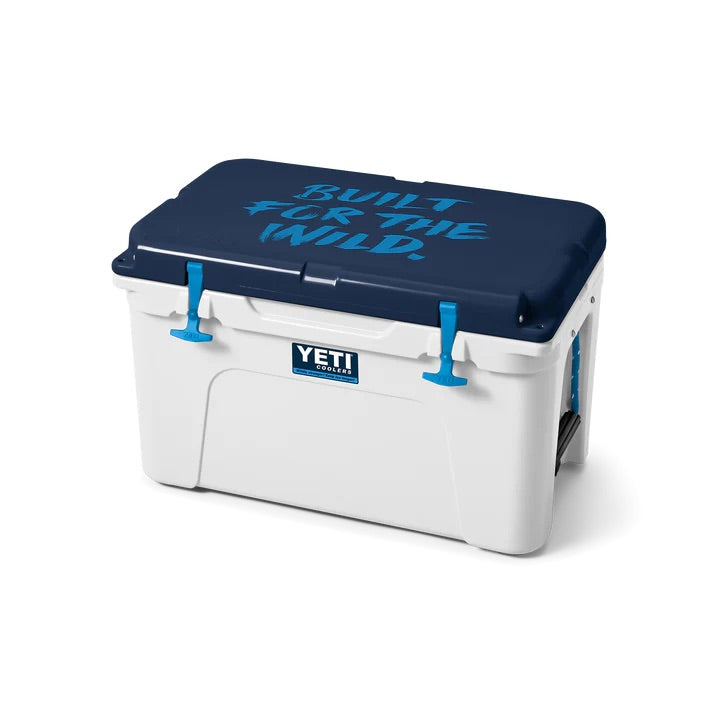 Die YETI® Kühlbox Tundra 45 - White/Blue hat einen weißen Korpus, einen dunkelblauen Deckel mit der Aufschrift "BUILT FOR THE WILD." in Blau, passende blaue Verschlüsse und das YETI-Logo auf der Vorderseite.