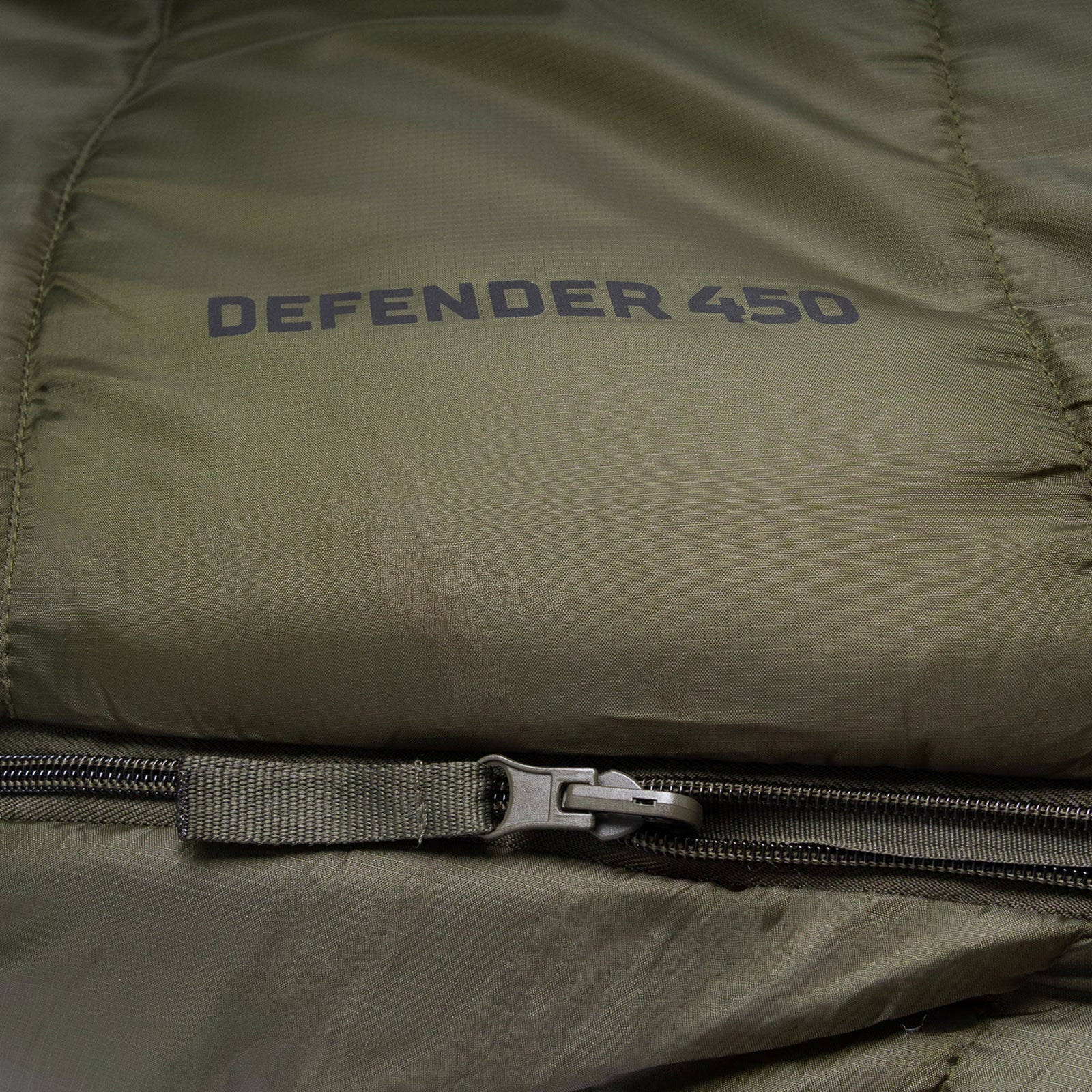 Nahaufnahme des olivgrünen Highlander Schlafsacks Defender 450 von HIGHLANDER OUTDOOR mit "DEFENDER 450"-Aufdruck und einem Reißverschluss im Bodenbereich - perfekt als vielseitiger 4-Jahreszeiten-Schlafsack für Ihr nächstes Outdoor-Abenteuer.