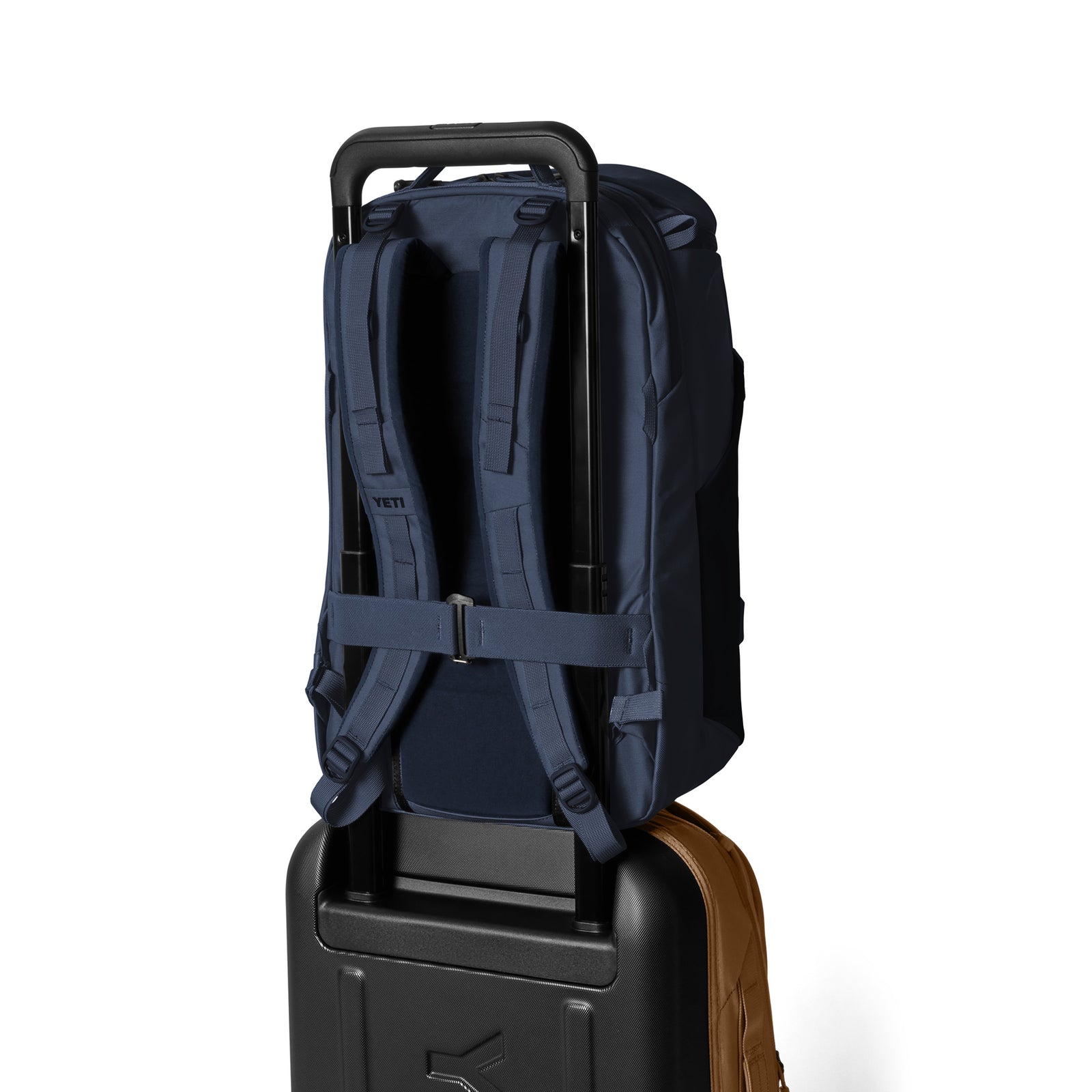 Der YETI® Rucksack Ranchero™ 27L in Classic Navy mit gepolsterten Trägern und einem Laptopfach sitzt mit dem Griff gesichert auf einem schwarzen Rollkoffer. Der Hintergrund ist einfarbig weiß.