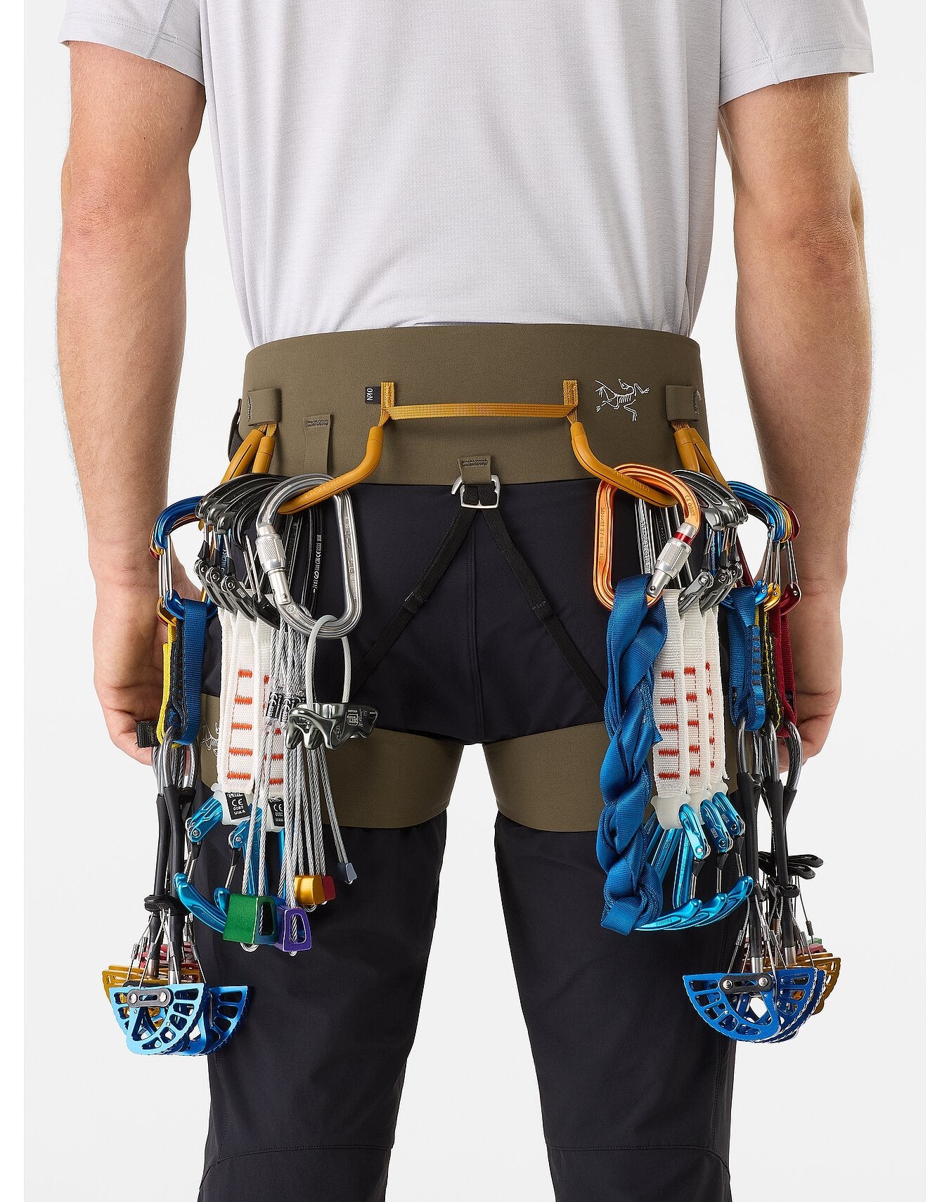 Eine Person, die ein ARC'TERYX LEAF Arc'teryx AR-395a Gurtzeug trägt, das mit Klemmgeräten, Karabinern, Expressschlingen und Schlingen beladen ist, von hinten gesehen vor einem schlichten Hintergrund.