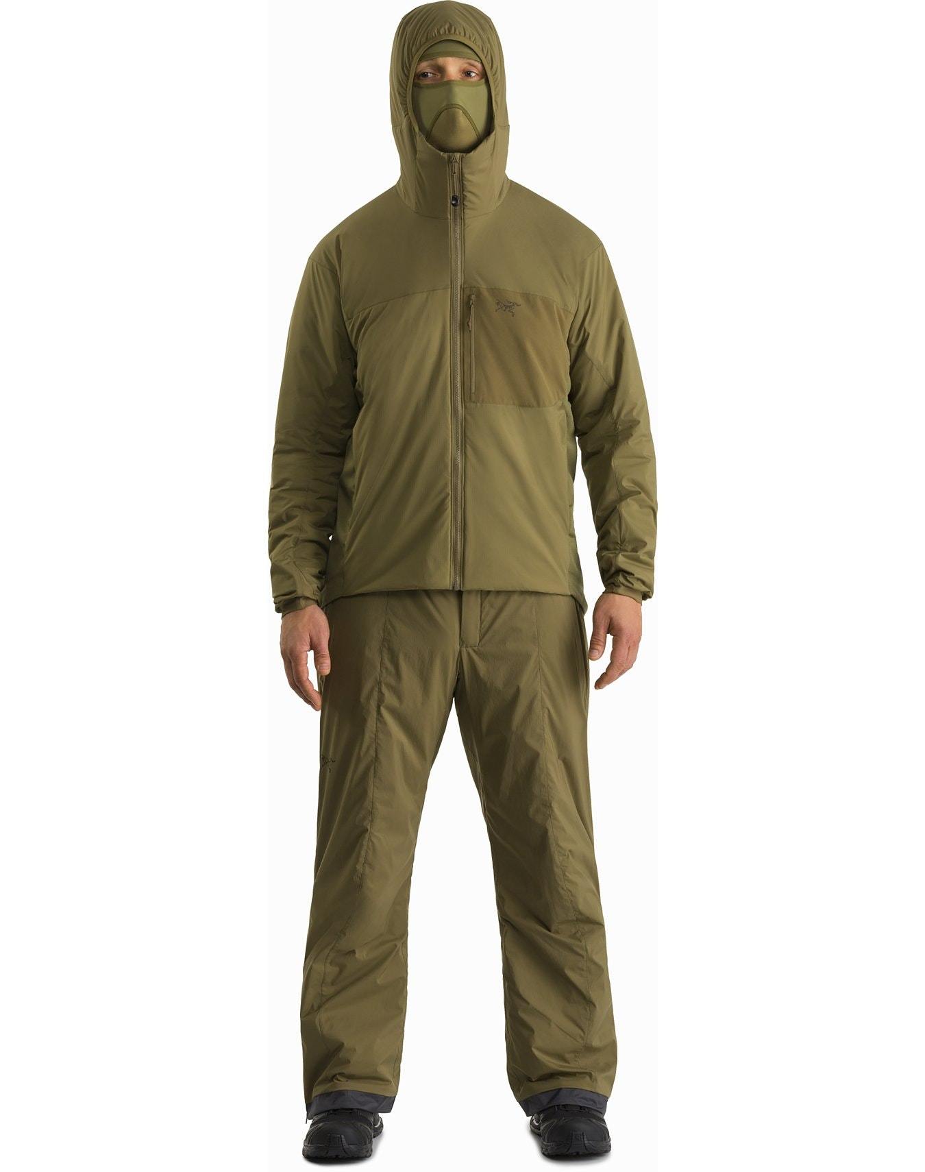 Eine Person steht mit dem ARC'TERYX LEAF Arc'teryx Atom Hoody LT Gen2.1 - Crocodile mit passender Hose, Gesichtsbedeckung, schwarzen Handschuhen und schwarzen Schuhen vor einem schlichten weißen Hintergrund.