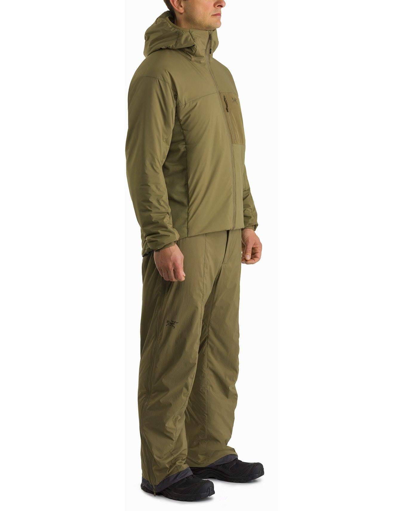 Eine Person im Profil trägt den ARC'TERYX LEAF Arc'teryx Atom Hoody LT Gen2.1 in Ranger Green mit passender Hose und schwarzen Schuhen und präsentiert damit leichte technische Oberbekleidung vor einem schlichten weißen Hintergrund.