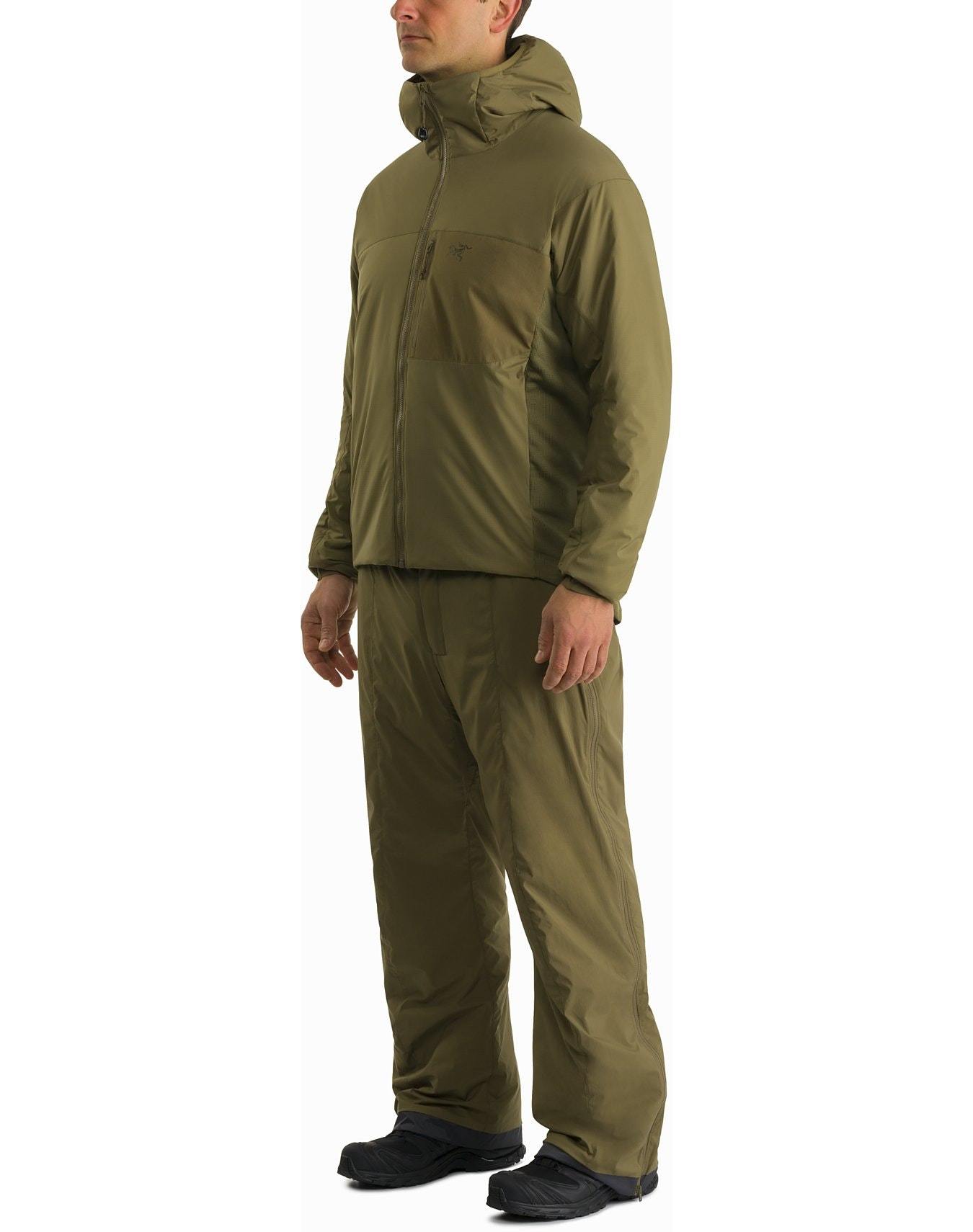 Eine Person trägt den ARC'TERYX LEAF Atom Hoody LT Gen2.1 in Ranger Green mit passender isolierter Hose und schwarzen Schuhen, ideal für kaltes Wetter, vor einem schlichten weißen Hintergrund.