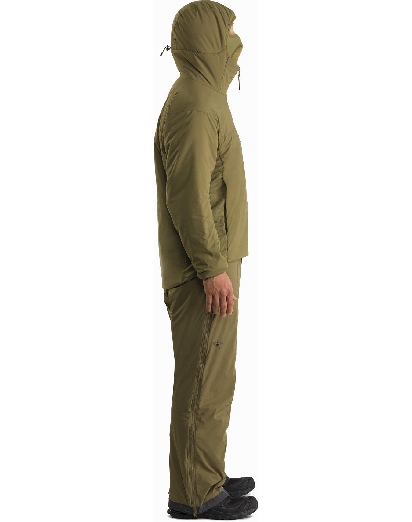 Ein Mann in einem grünen Arc'teryx Atom Hoody LT Gen2.1 - Wolf von ARC'TERYX LEAF steht selbstbewusst da und unterstreicht den eleganten Stil und den Komfort dieser leichten Isolationsjacke.