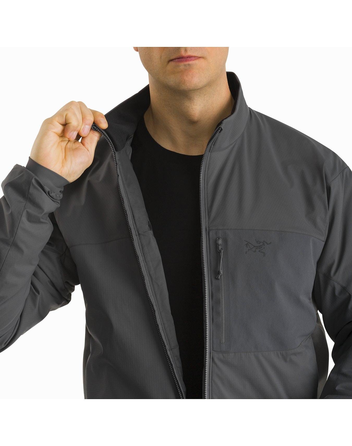 Eine Person, die eine ARC'TERYX LEAF Arc'teryx Atom Jacket LT Gen2.1 in Ranger Green über einem schwarzen Hemd trägt, schließt den Reißverschluss der Jacke, wobei nur ihr Oberkörper zu sehen ist und der Kopf teilweise aus dem Rahmen fällt.
