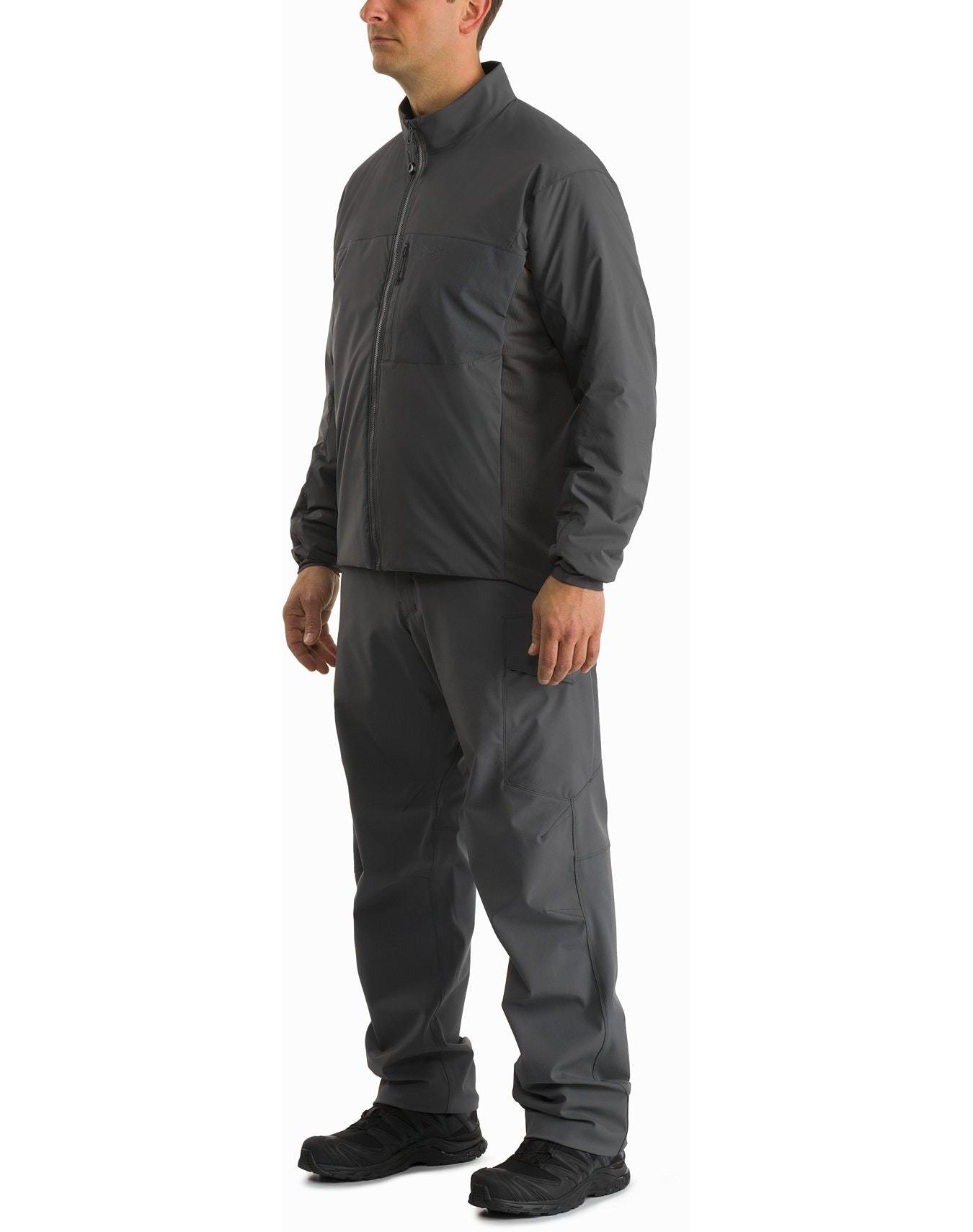 Eine Person steht mit Blick nach links und trägt eine ARC'TERYX LEAF Arc'teryx Atom Jacket LT Gen2.1 in Ranger Green mit passender Hose und schwarzen Schuhen vor einem schlichten weißen Hintergrund.