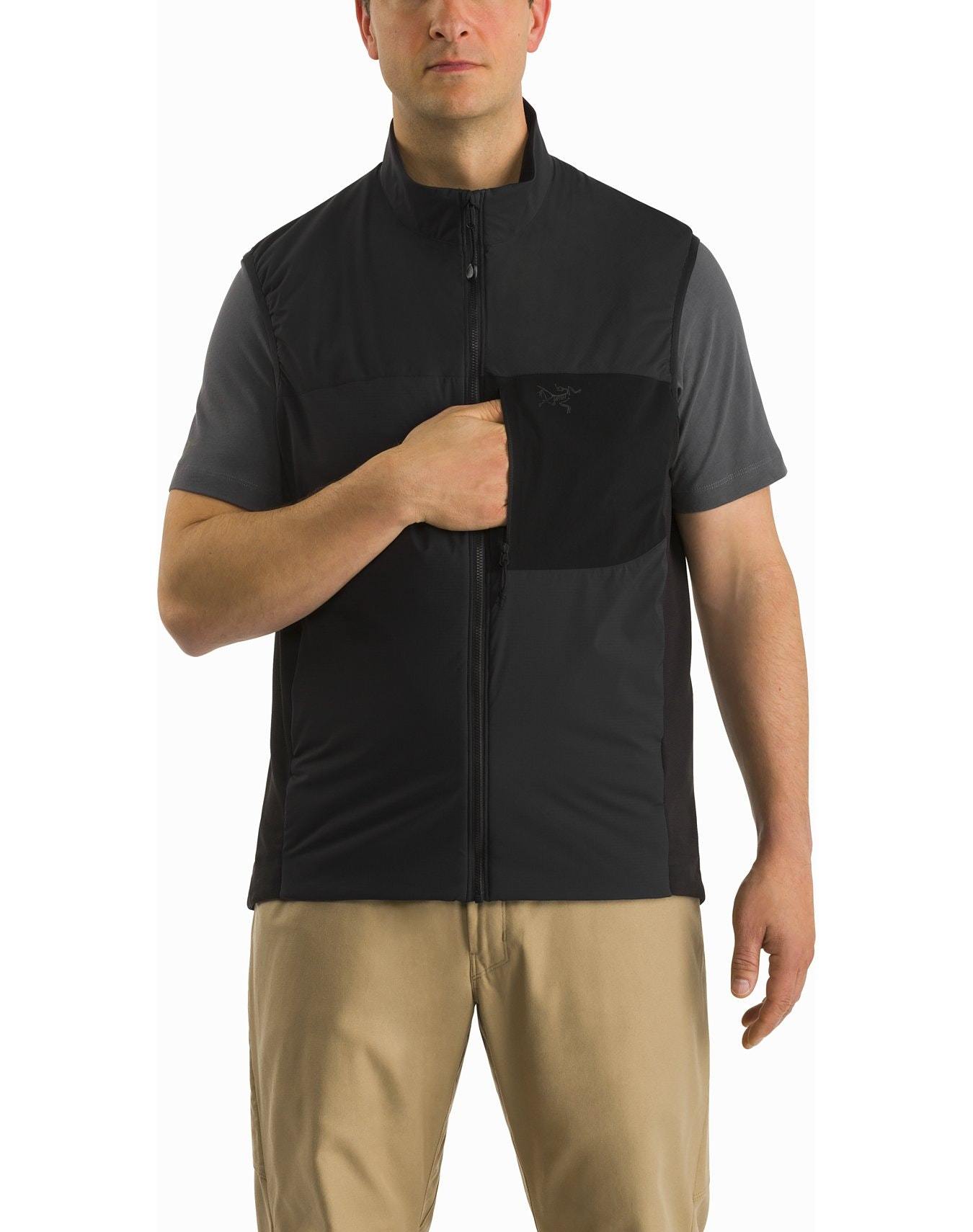 Ein Mann trägt eine ARC'TERYX LEAF Arc'teryx Atom Vest LT Gen2.1 - Wolf über einem grauen kurzärmeligen Hemd und einer hellbraunen Hose. Er steht vor einem weißen Hintergrund und hat eine Hand in der Brusttasche der Weste.