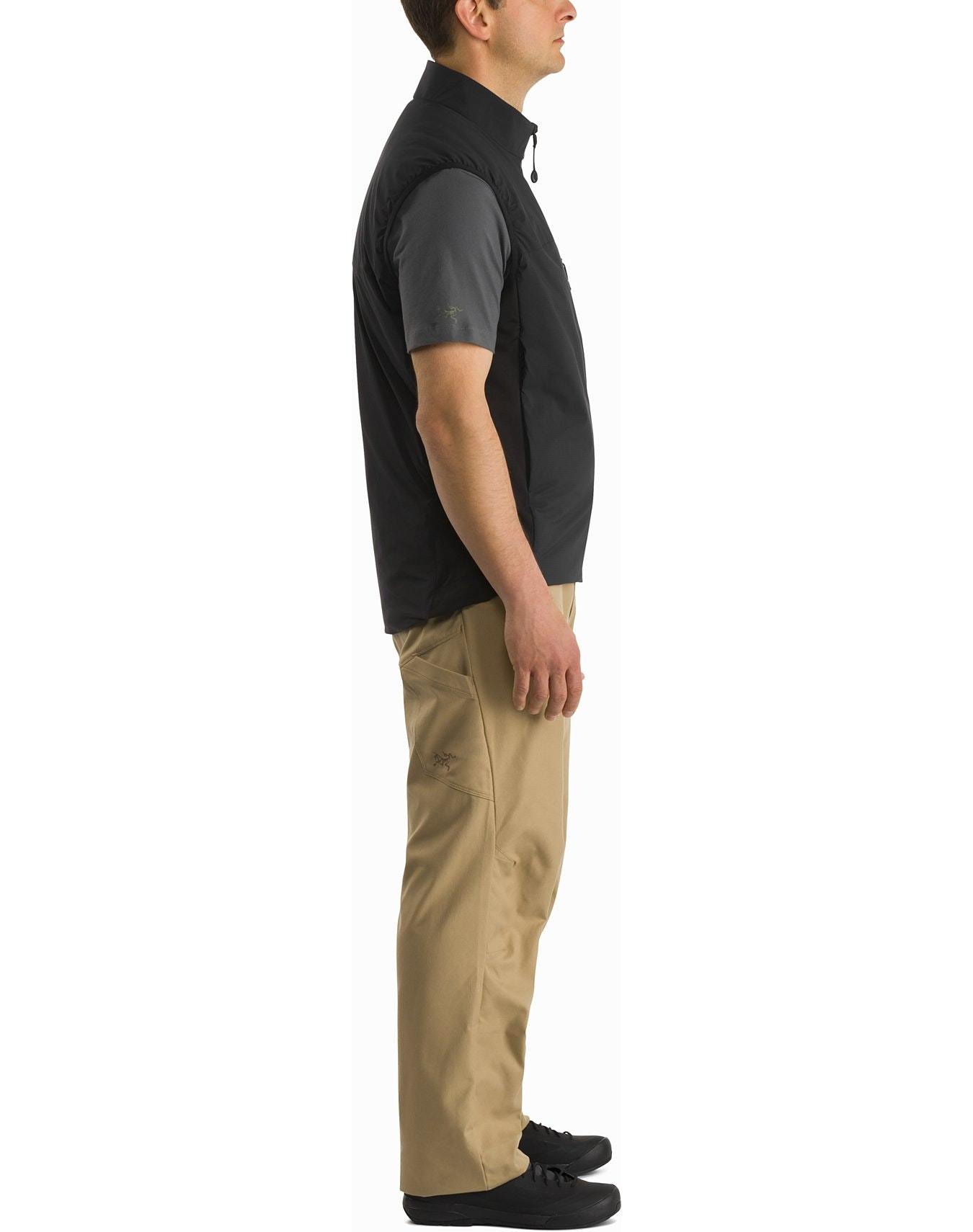 Ein Mann im Profil trägt ein graues Hemd, die ARC'TERYX LEAF Arc'teryx Atom Vest LT Gen2.1 - Wolf, eine beige Hose und schwarze Schuhe vor einem weißen Hintergrund.