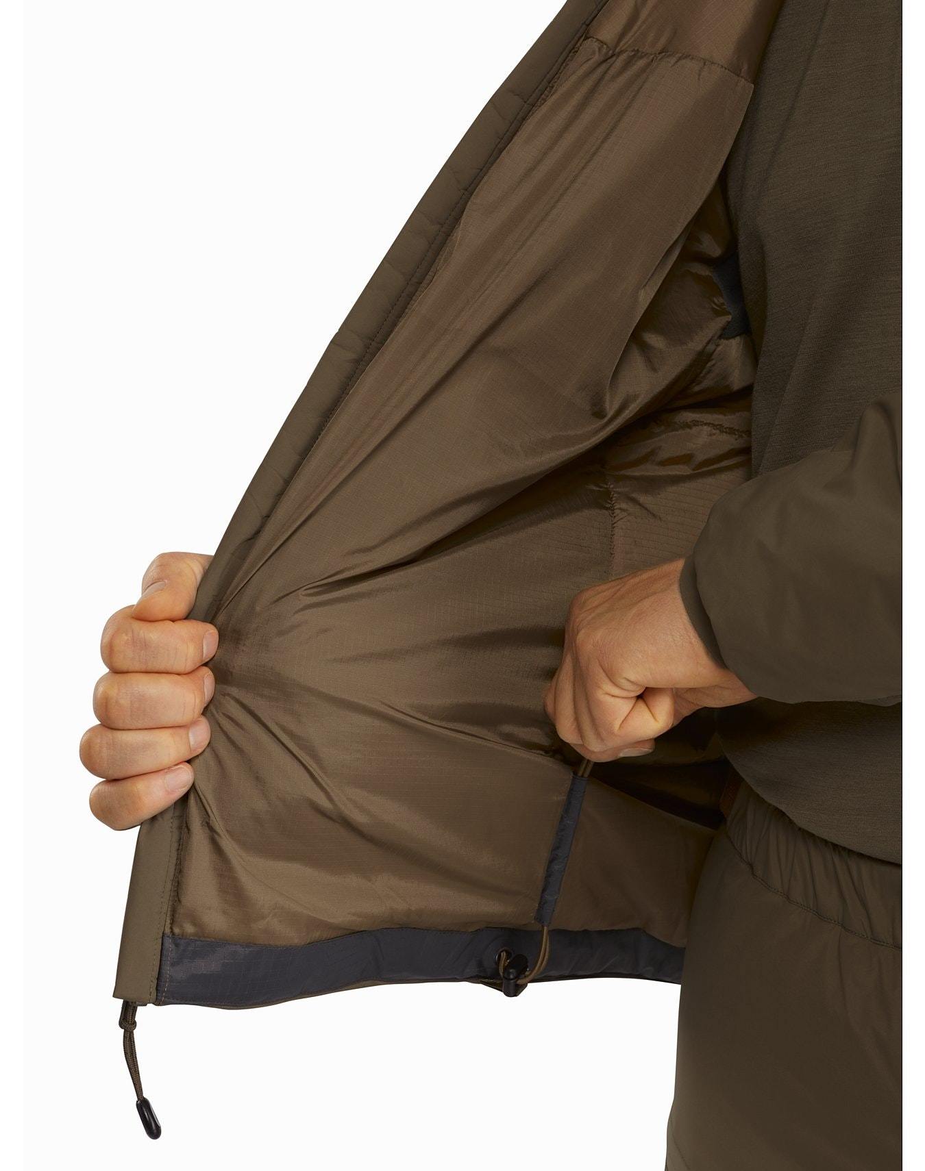 Eine Person in einem rangergrünen ARC'TERYX LEAF Cold WX Hoody LT Gen2.1 hält eine Seite offen, um das Innenfutter und eine Innentasche zu zeigen, wobei nur die Jacke und ihre Hände sichtbar sind.