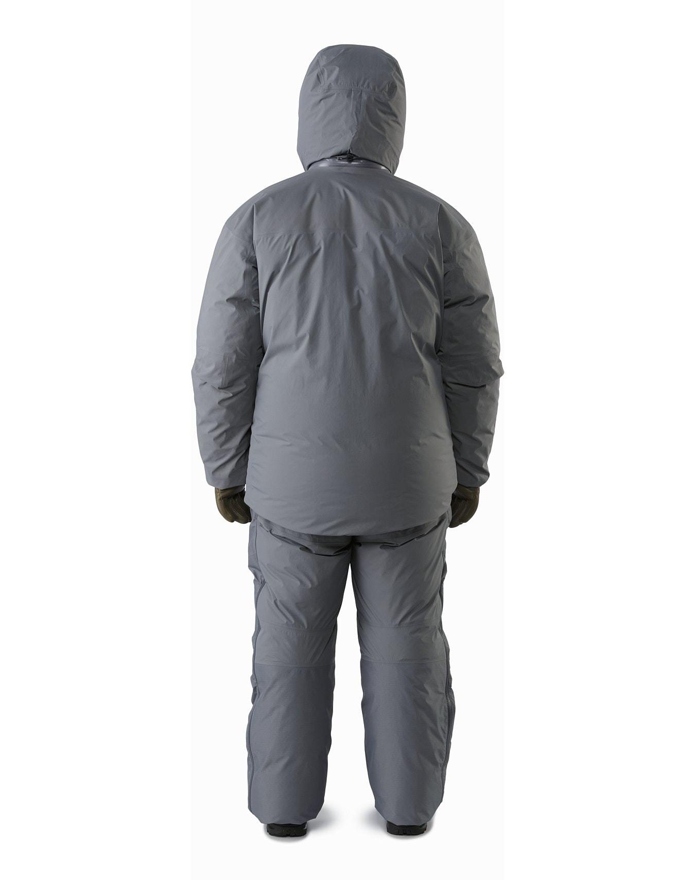 Eine Person steht mit dem Arc'teryx Cold WX Parka SVX - Wolf von ARC'TERYX LEAF und einer passenden isolierten Hose vor dem Hintergrund. Ihre Hände, in dunklen Handschuhen, ruhen an der Seite vor einem schlichten weißen Hintergrund.