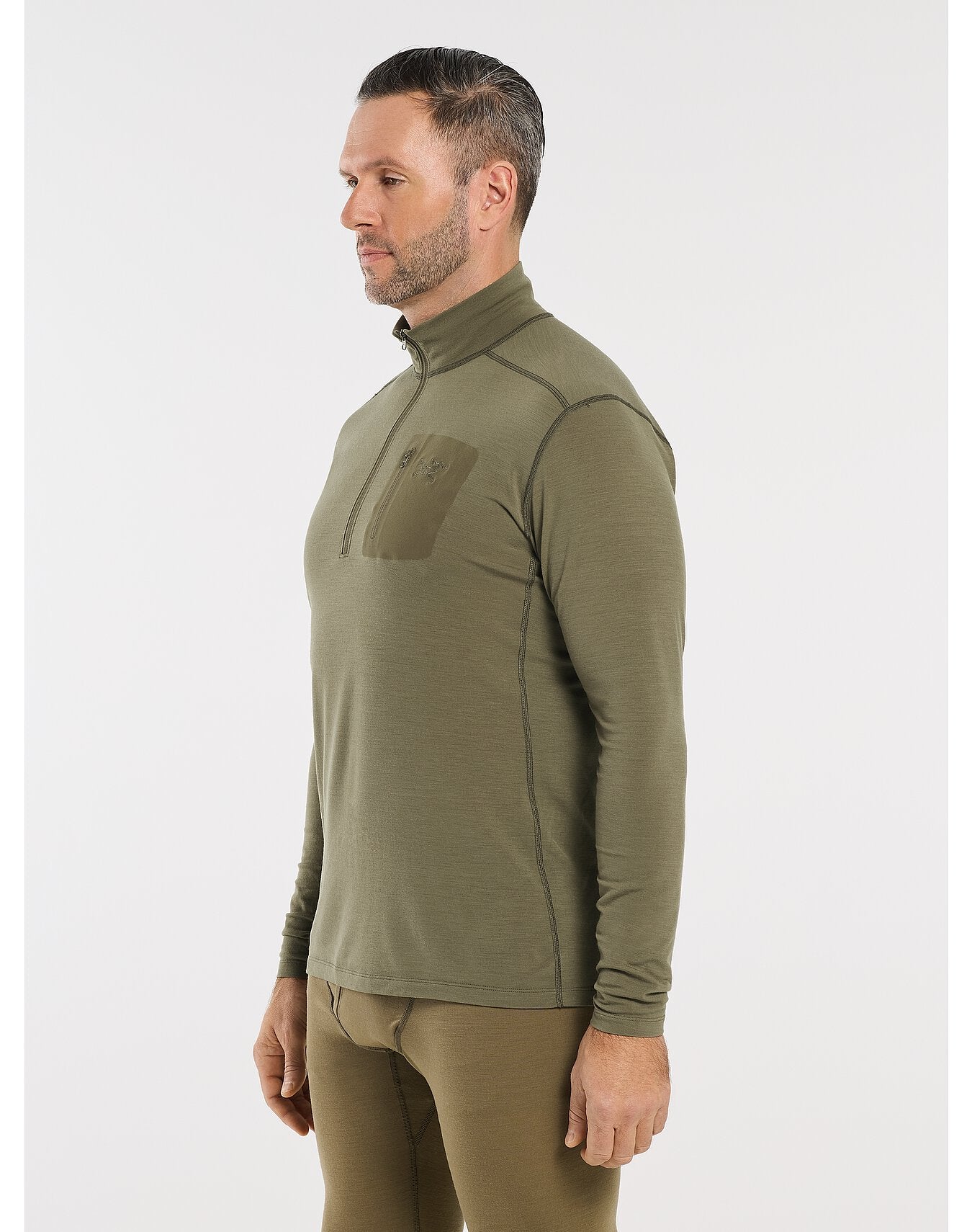 Mann in einem olivgrünen ARC'TERYX LEAF Cold WX Zip Neck AR - Crocodile mit Brustaufnäher und Kontrastnähten, gepaart mit einer passenden Base Layer Hose, von der Seite gesehen.