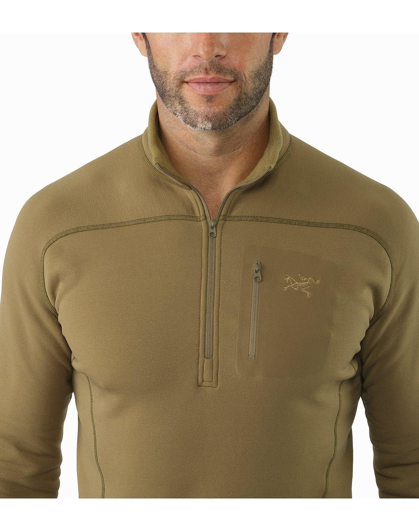 Ein Mann trägt einen ARC'TERYX LEAF Cold WX Zip Neck SV - Crocodile Baselayer aus POLARTEC-Fleece mit einer Brusttasche mit Reißverschluss und einem kleinen Logo an der linken Seite. Nur sein Oberkörper und sein Gesicht sind zu sehen.
