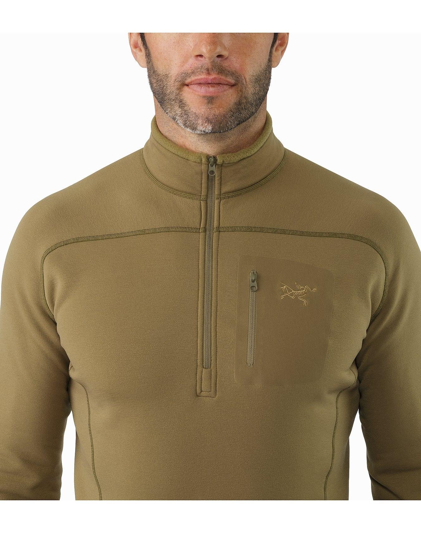 Ein Mann trägt einen olivgrünen ARC'TERYX LEAF Cold WX Zip Neck SV - Crocodile Pullover mit Brusttasche und gesticktem Logo aus POLARTEC Fleece, dargestellt von den Schultern bis zum Mund vor weißem Hintergrund.