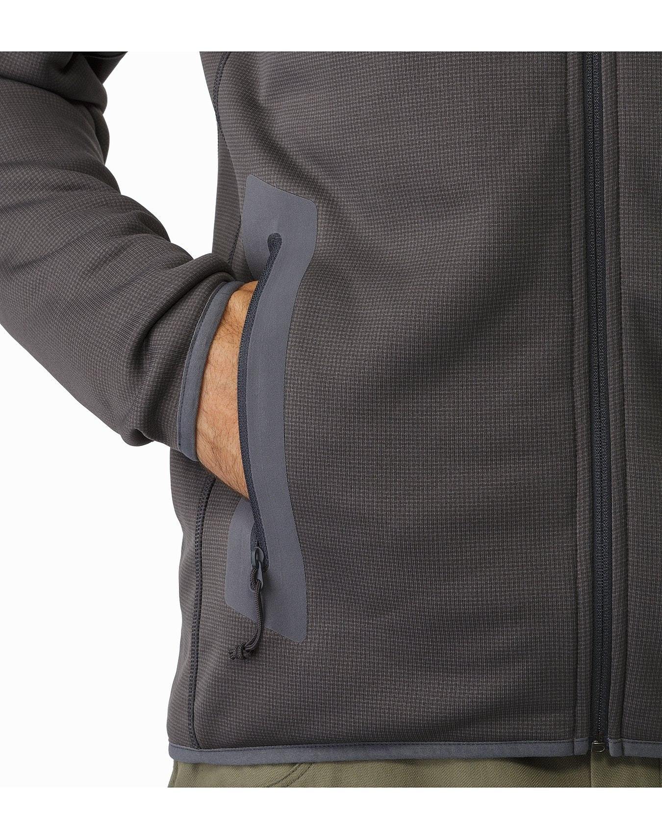 Eine Person trägt einen schwarzen ARC'TERYX LEAF Arc'teryx Naga Hoody Full Zip Gen2.1, die Hand in einer Seitentasche mit Reißverschluss, dargestellt von der Brust abwärts vor einem schlichten weißen Hintergrund.