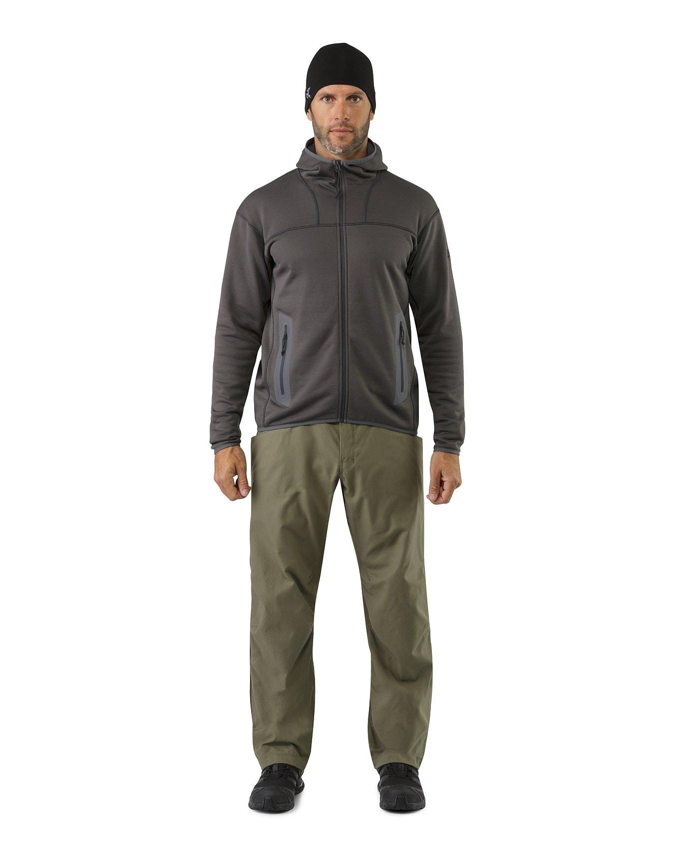 Ein Mann sieht nach vorne, trägt einen ARC'TERYX LEAF Arc'teryx Naga Hoody Full Zip Gen2.1 in Ranger Green, eine schwarze Mütze, eine olivgrüne Hose und schwarze Schuhe und steht vor einem schlichten weißen Hintergrund.