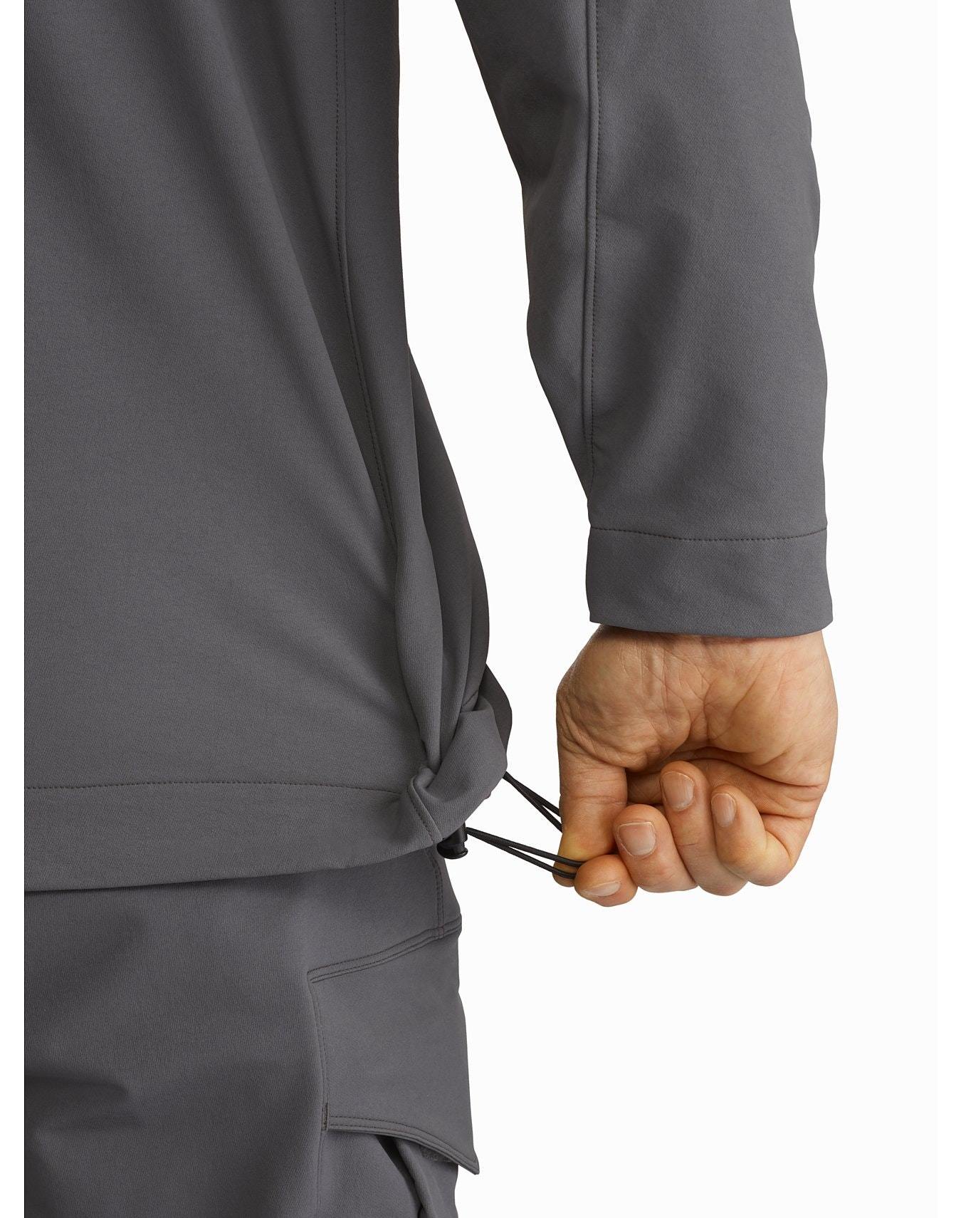 Die Hand einer Person verstellt einen schwarzen Kordelzug am Saum der ARC'TERYX LEAF Arc'teryx Patrol Jacket AR Men's in Schwarz. Nur der untere Teil der Jacke, der Ärmel und die Hose sind vor einem weißen Hintergrund zu sehen.