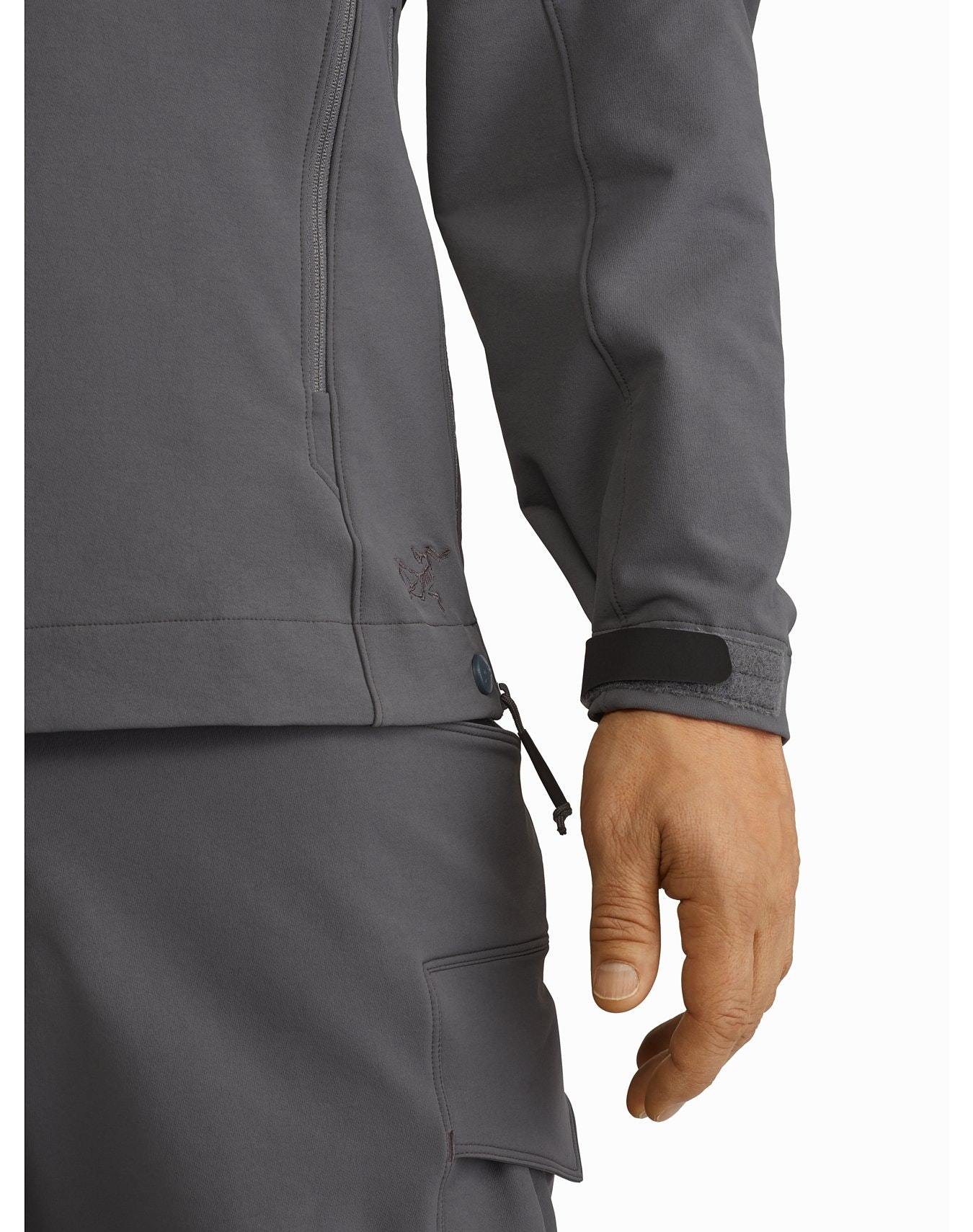 Eine Person, die die ARC'TERYX LEAF Arc'teryx Patrol Jacket AR Men's - Wolf trägt, zeigt eine Nahaufnahme ihrer rechten Hand und ihres Arms. Die Jacke hat ein kleines Logo, sichtbare Nähte, eine Tasche und ein schwarzes, verstellbares Manschettenband.