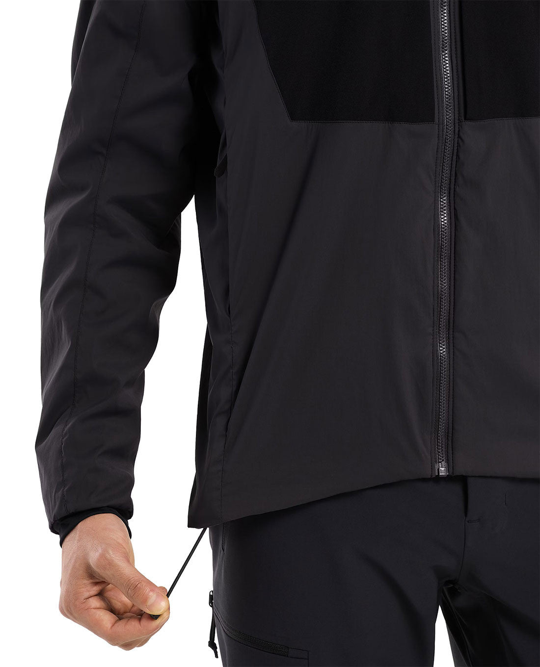 Eine Person in einem schwarzen ARC'TERYX PRO Practitioner AR Hoody Men's - Carbon Copy verstellt mit der linken Hand den Taillenkordelzug. Das Bild zeigt die Seite und einen Teil der Vorderseite dieses atmungsaktiven Midlayers, mit Fokus auf die Saumverstellung.