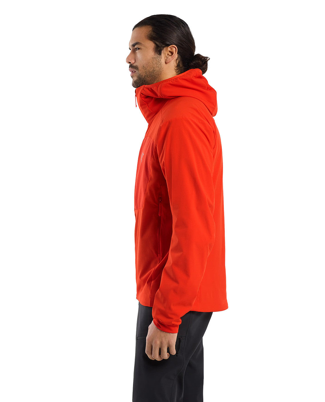 Ein Mann mit langen dunklen Haaren, die nach hinten gebunden sind, trägt ein leuchtend orangefarbenes ARC'TERYX PRO Arc'teryx Practitioner AR Hoody Men's - Dynasty und eine schwarze Hose. Er steht im Profil vor einem schlichten weißen Hintergrund.