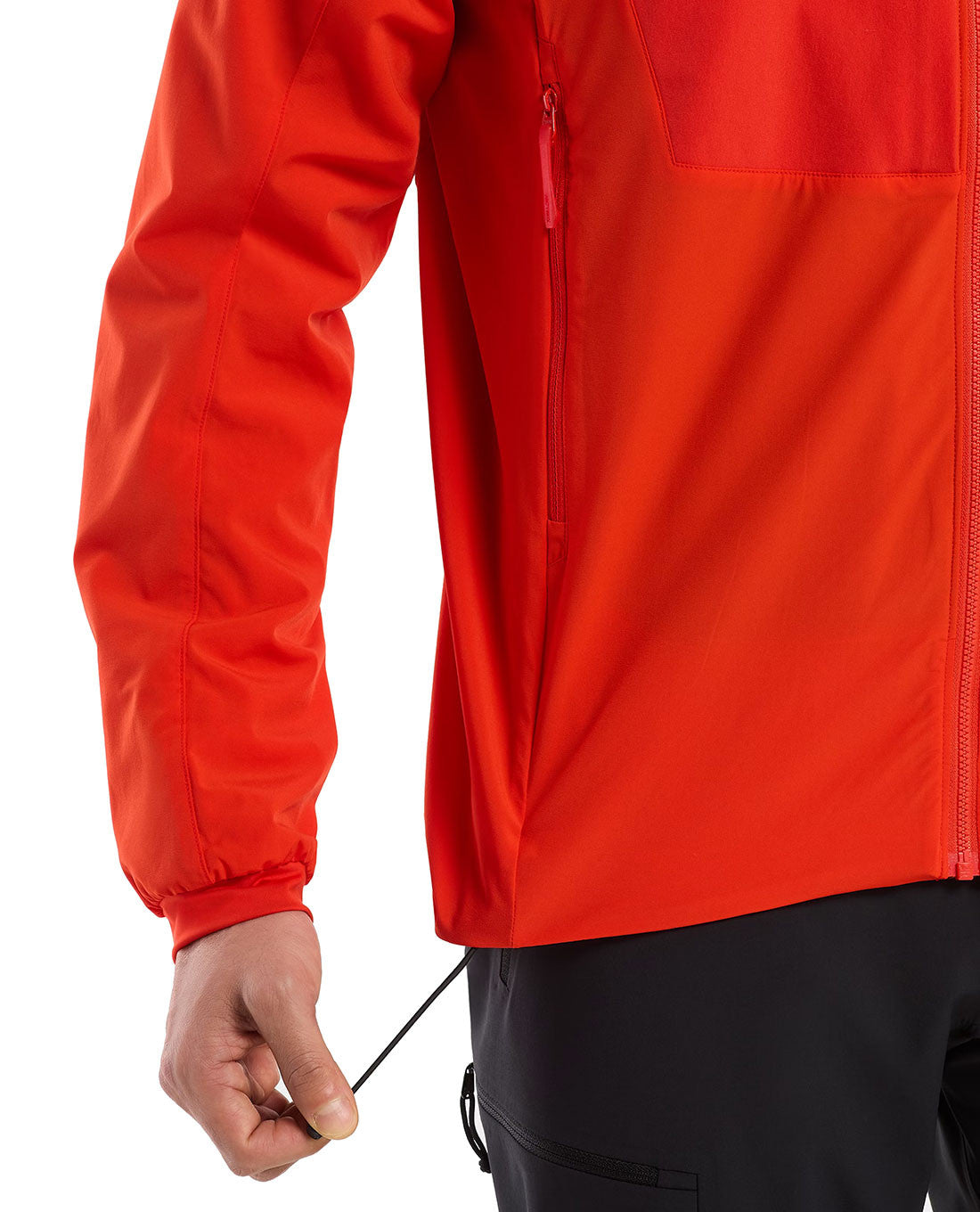 Eine Person in einem leuchtend roten ARC'TERYX PRO Arc'teryx Practitioner AR Hoody Men's - Dynasty verstellt mit einer Hand den Kordelzug am Saum. Das Foto zeigt nur den Torso und einen Teil eines Arms, gepaart mit einer schwarzen Hose.