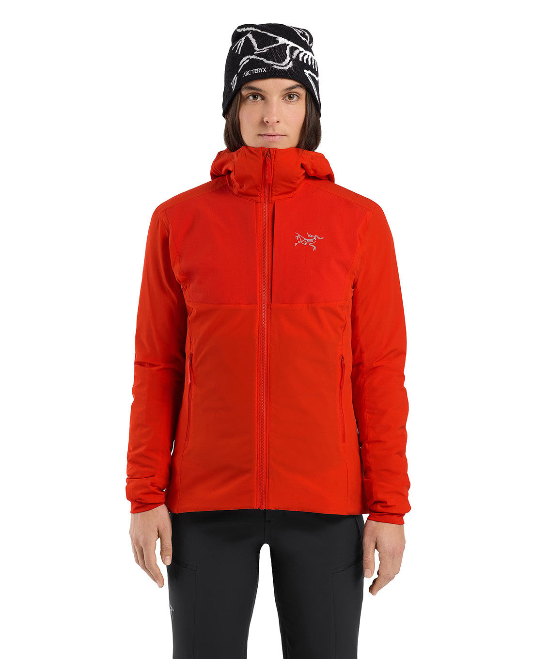 Eine Person in der ARC'TERYX PRO Arc'teryx Practitioner AR Hoody Women's - Dynasty, leuchtend rot, und einer schwarzen Mütze mit weißen Motiven steht mit dem Gesicht nach vorne vor einem weißen Hintergrund und präsentiert diese atmungsaktive Isolationsjacke.
