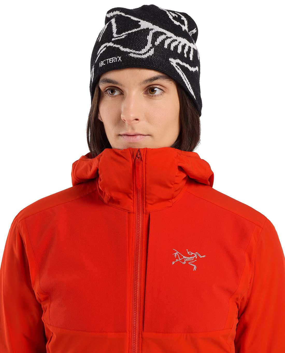 Eine Person mit schwarzer Mütze mit weißer Grafik trägt die ARC'TERYX PRO Arc'teryx Practitioner AR Hoody Women's - Dynasty, eine atmungsaktive Isolationsjacke mit dem weißen Arcteryx-Logo auf der Brust, und schaut leicht zur Seite.