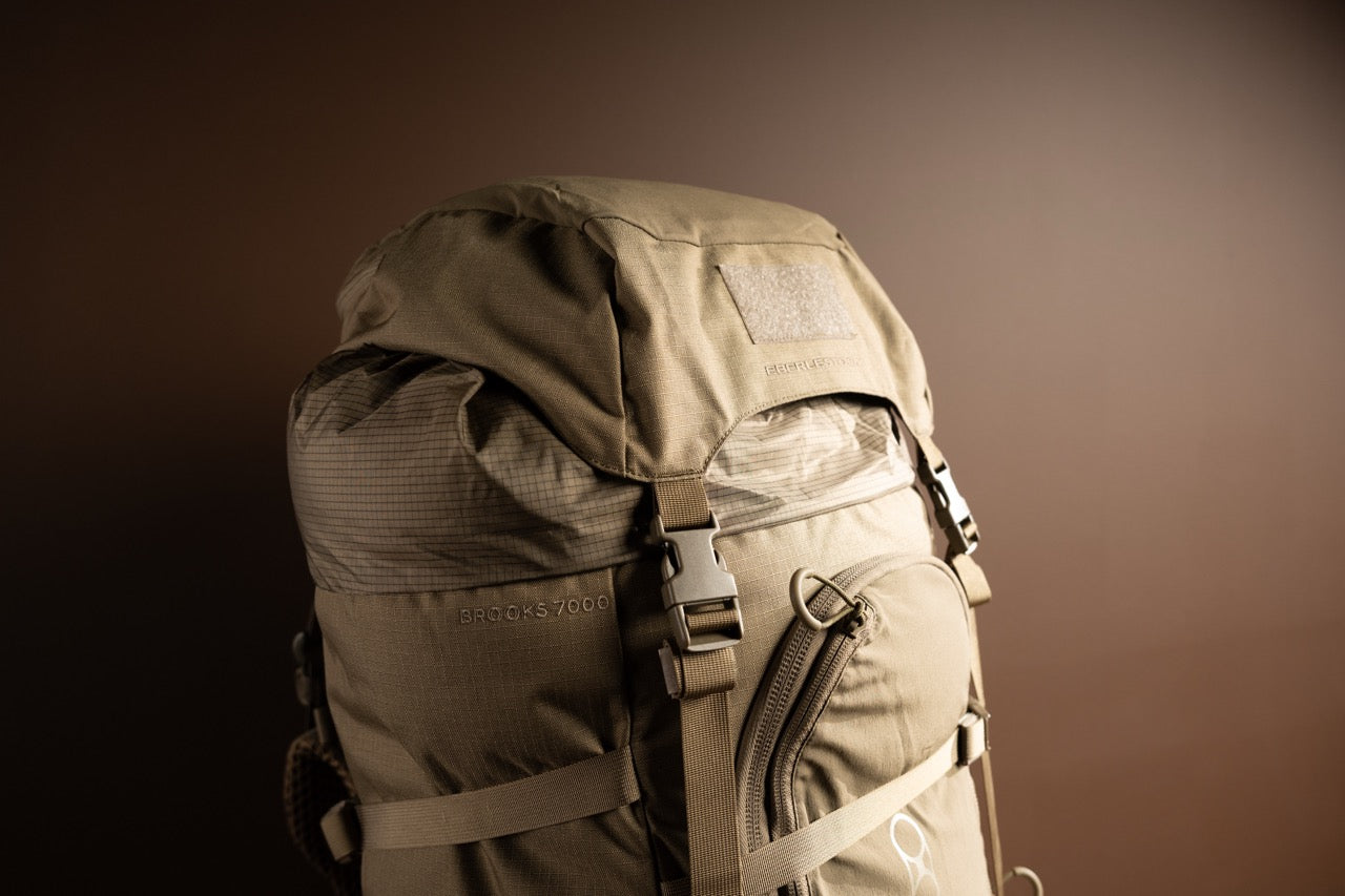 Ein EBERLESTOCK Brooks 7000 Wanderrucksack in Militärgrün mit mehreren Fächern, stabilen Riemen und Schnallen ist vor einem einfarbig braunen Hintergrund abgebildet. Dieser modulare Rucksack hat einen robusten Look, ideal für den Einsatz im Freien.